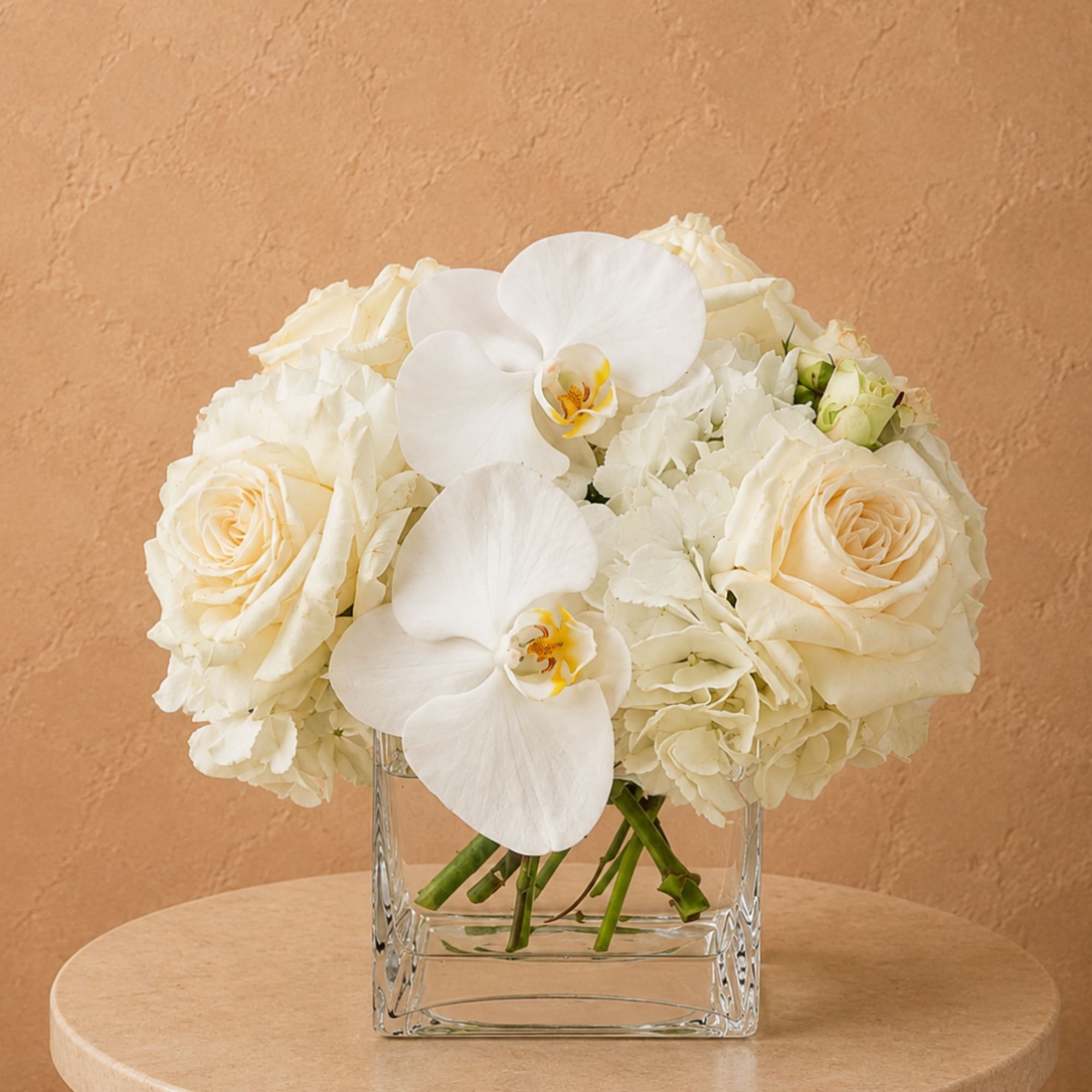 White roses and orchids arranged in a clear square vase