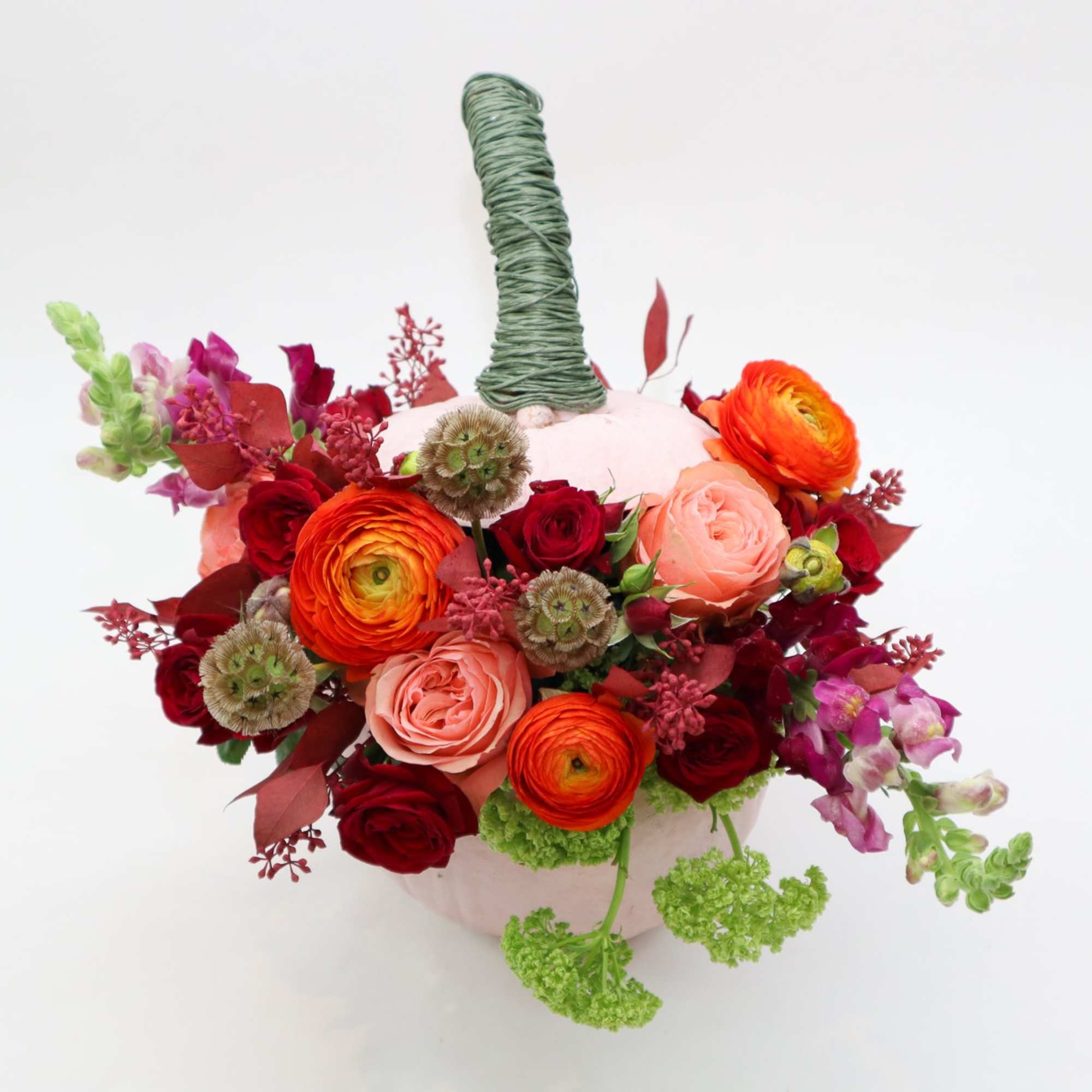 Mixed bouquet in a pale vase with orange, red, and pink blooms