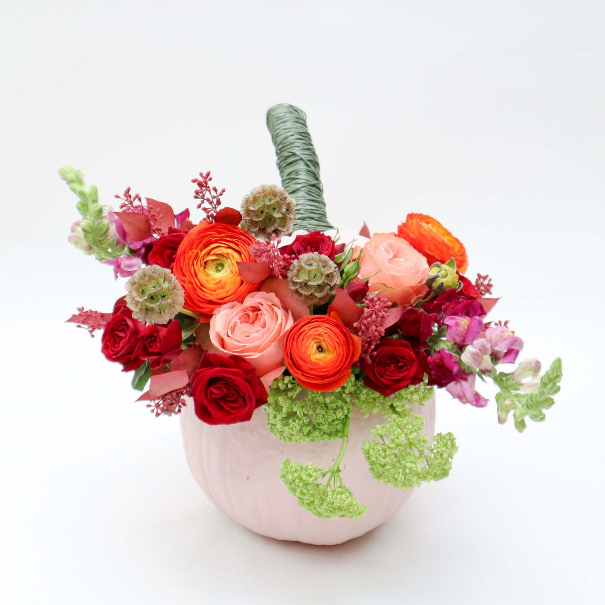 Mixed bouquet of red, pink, and orange flowers in a pale pink vase