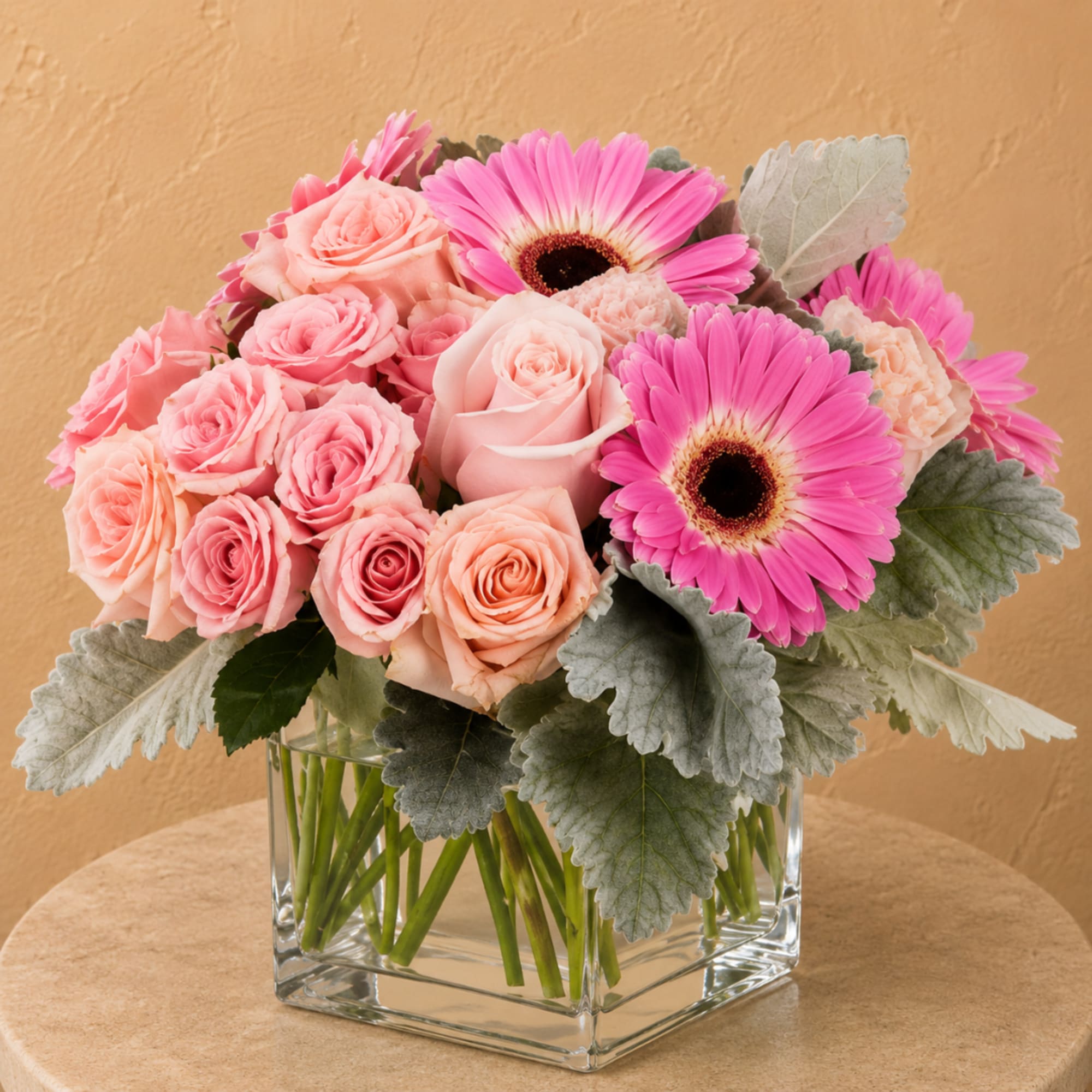Pink roses and gerbera daisies in a clear square vase