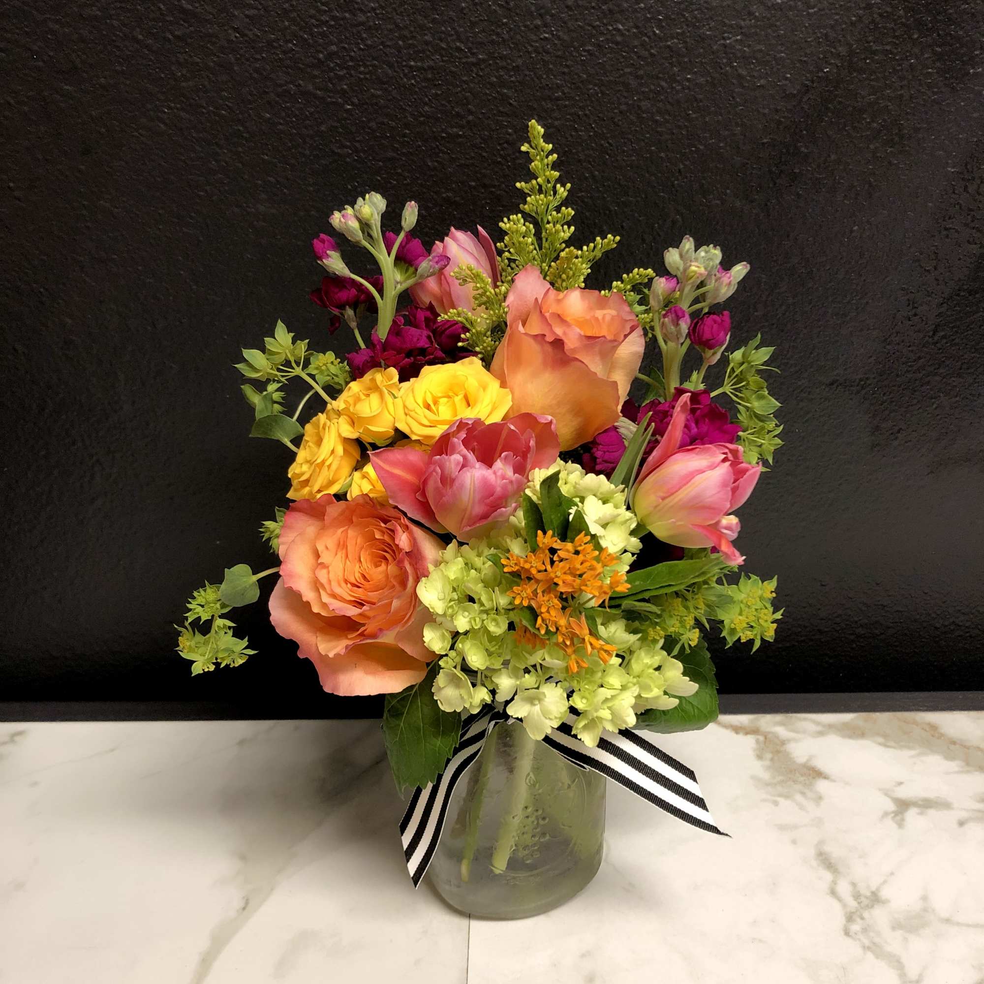 Colorful bouquet of roses and tulips in a glass vase with a striped ribbon