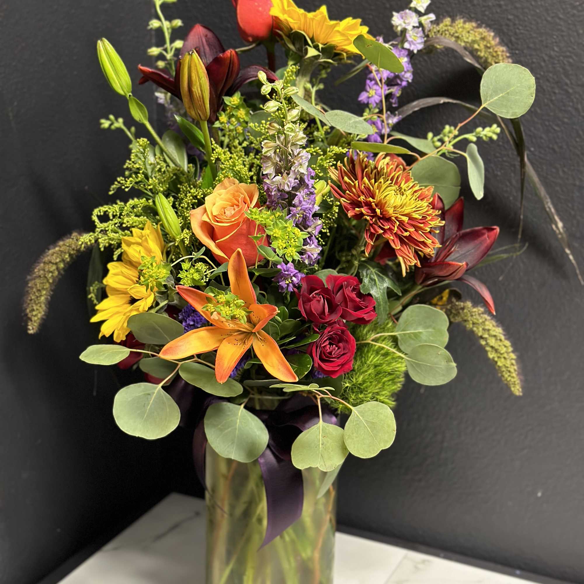 Mixed bouquet in a glass vase with roses, lilies, and sunflowers