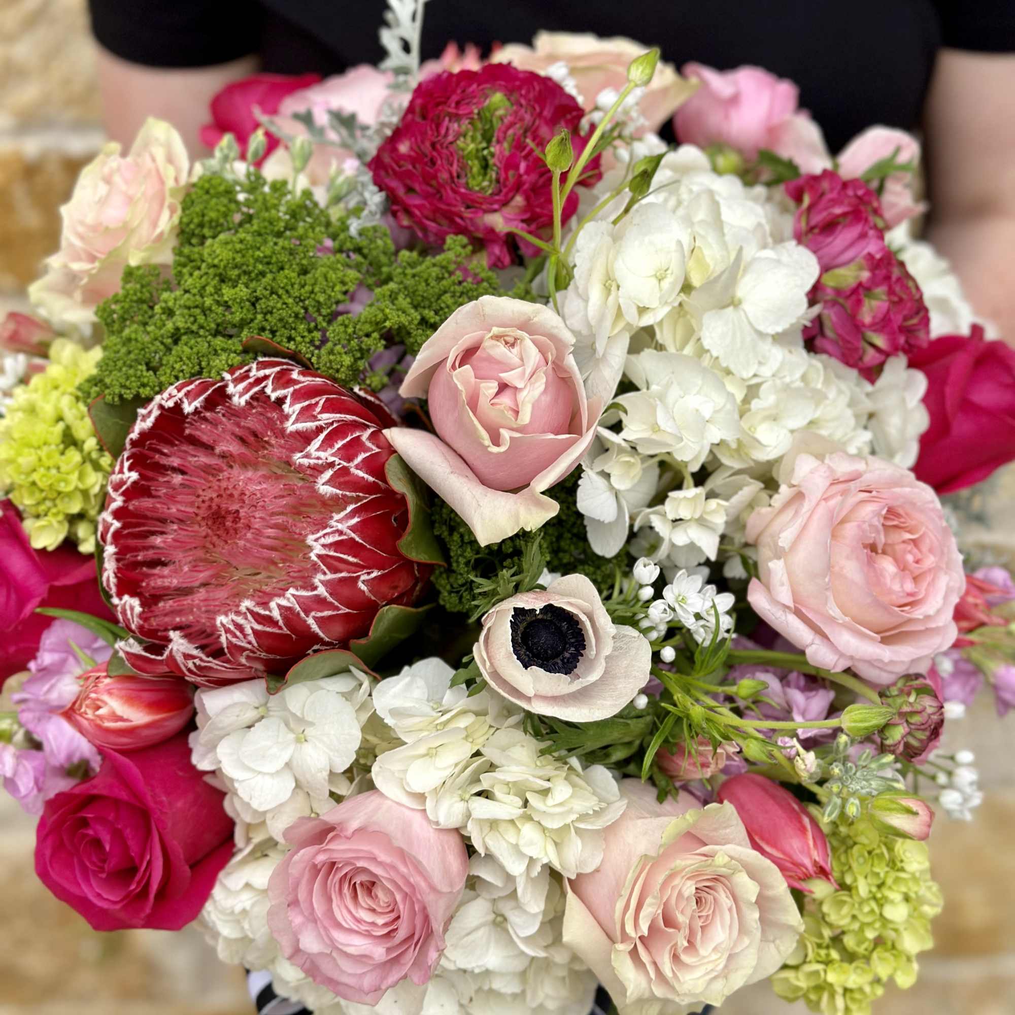 Handheld bouquet of pink and white flowers with a large red protea