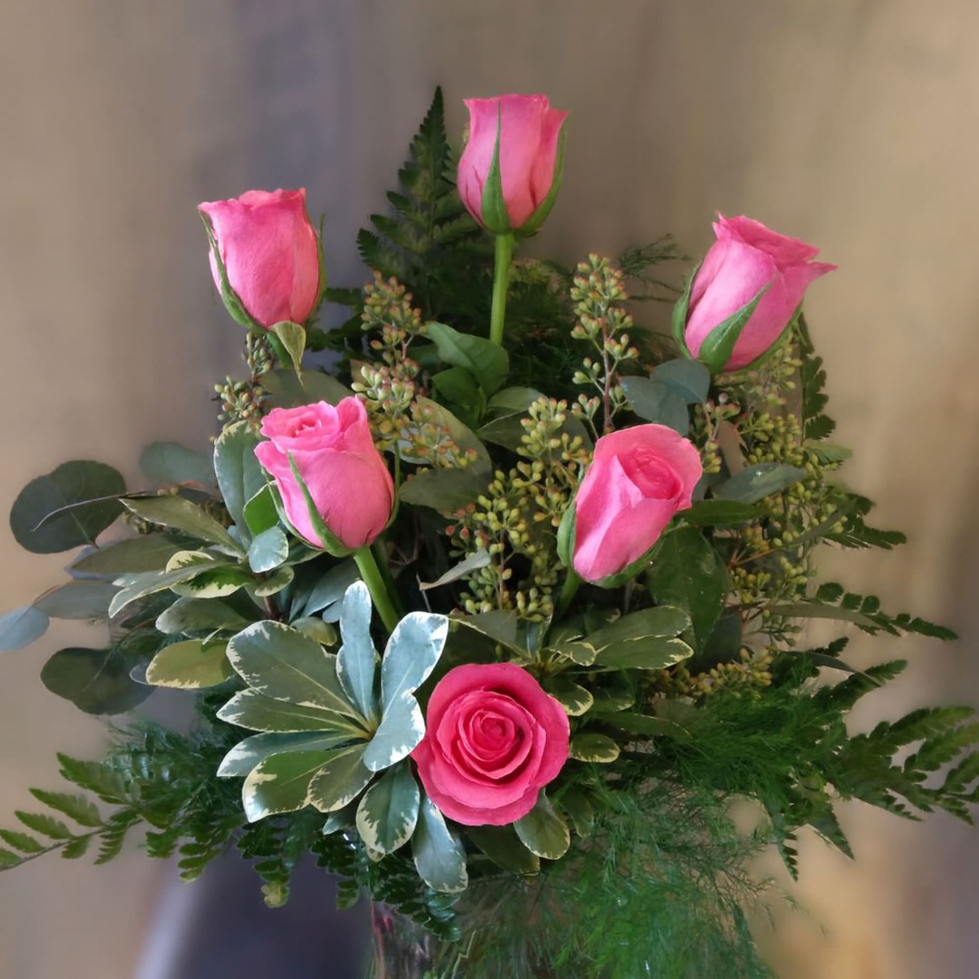 Pink roses in a glass vase with mixed greenery