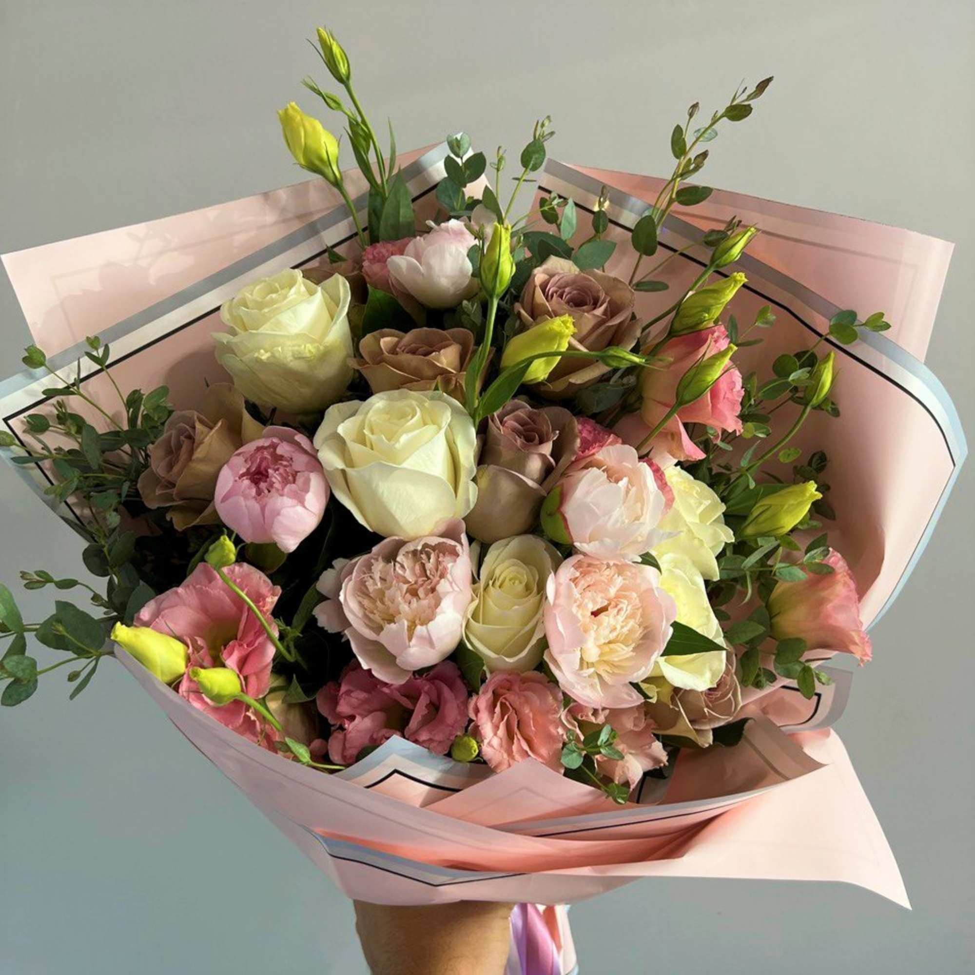 Hand-tied bouquet of pink and cream roses and peonies wrapped in pink paper