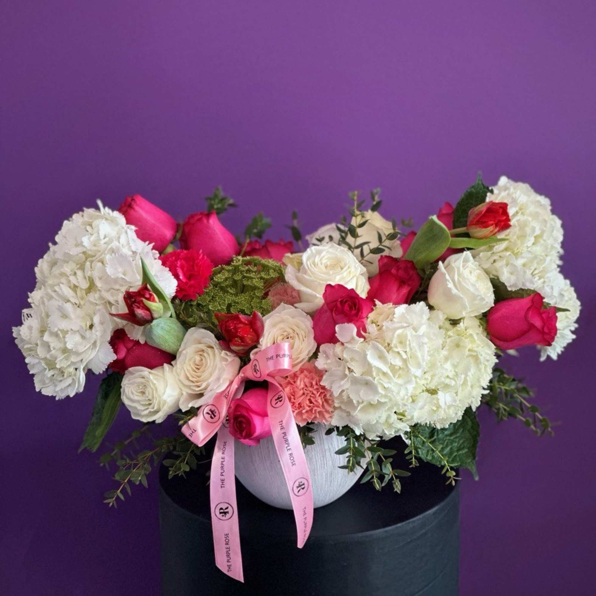 Low arrangement of white hydrangeas with pink and white roses in a white bowl with a pink ribbon.