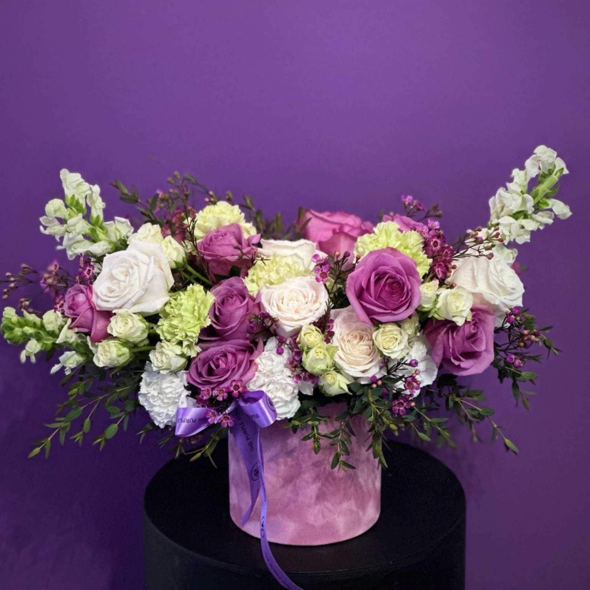 Round hat box arrangement of purple and white roses with green carnations and filler flowers