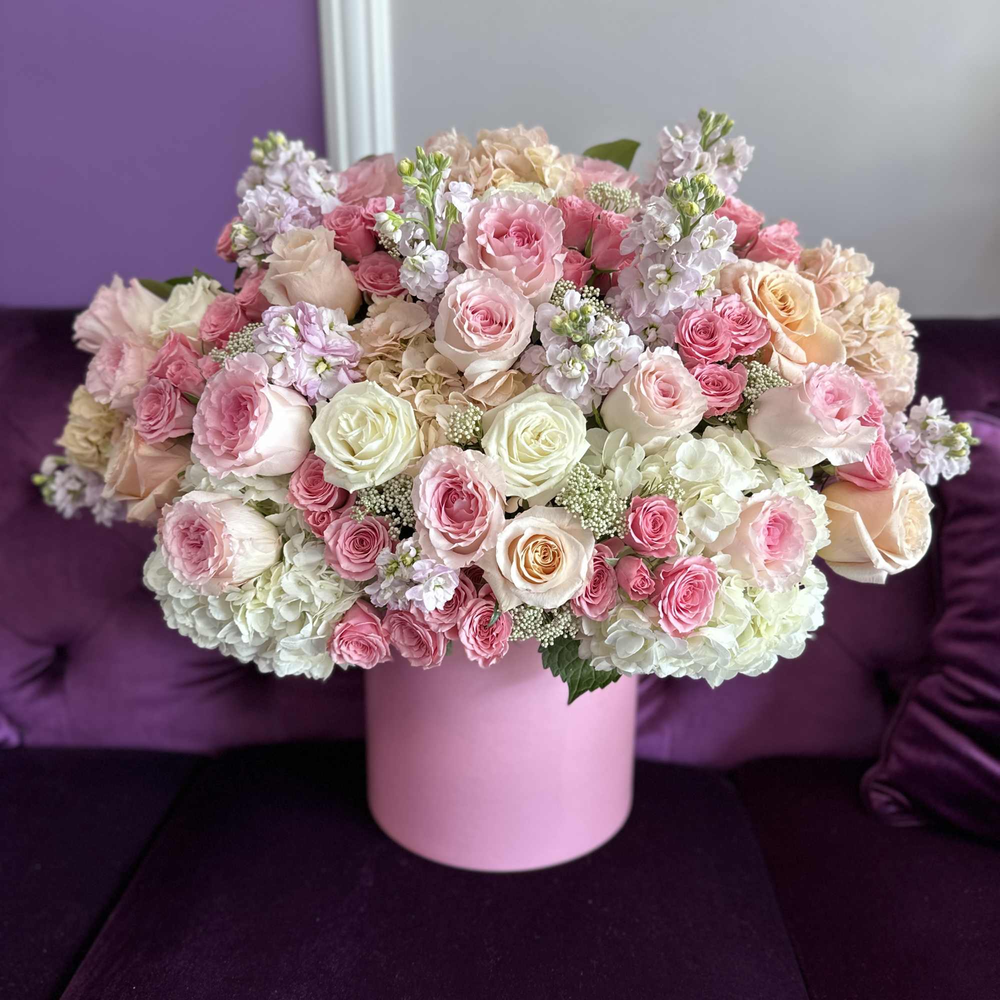 Low lush arrangement of pink, peach, and cream roses with hydrangeas in a round pink box.