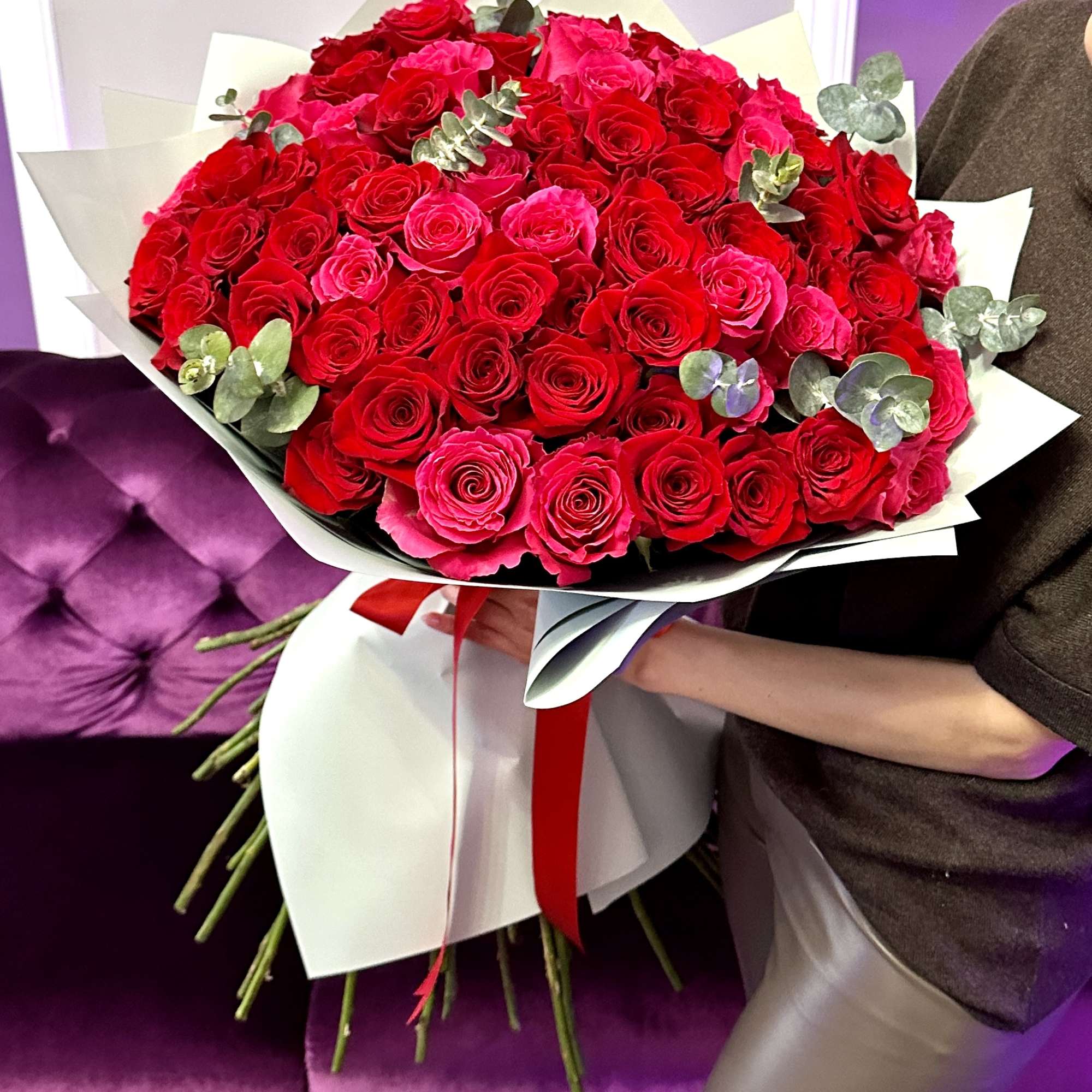 Large hand-tied bouquet of red and hot pink roses wrapped in white paper with a red ribbon.