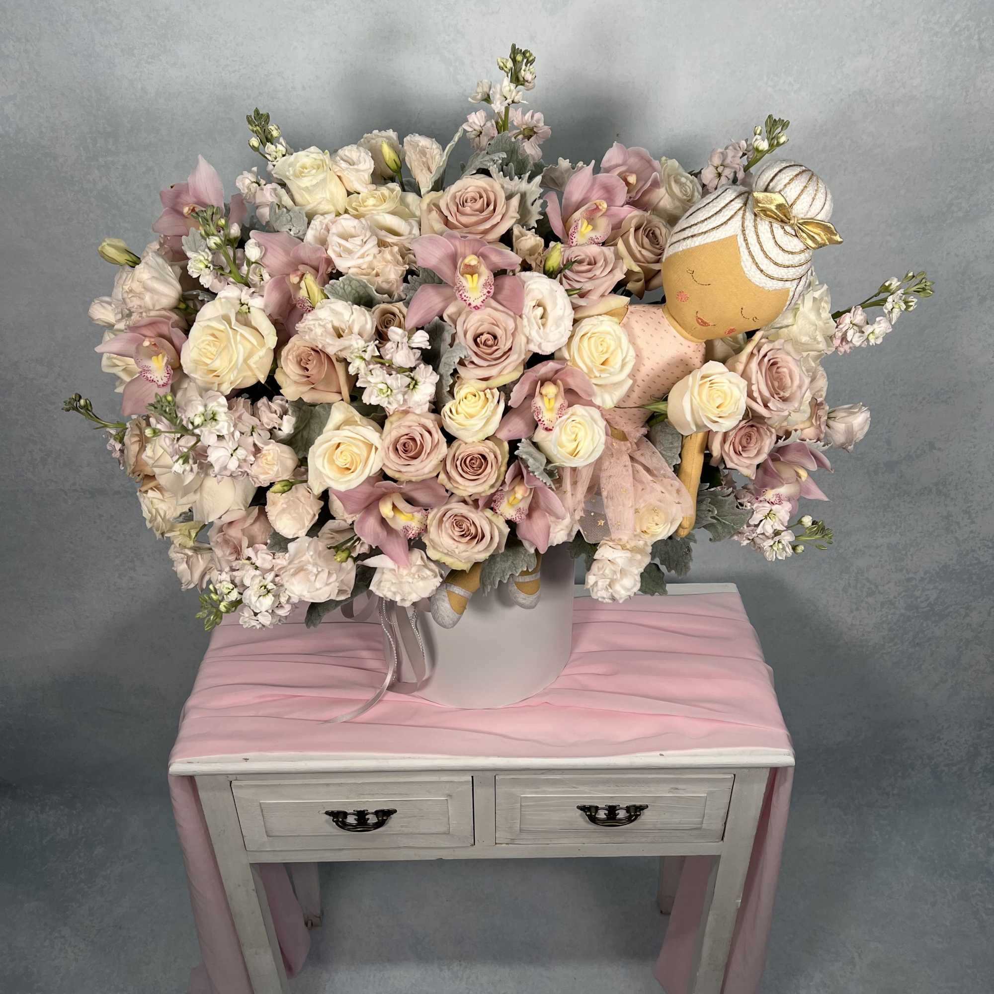 Large pastel bouquet of roses and orchids in a white hatbox with a ballerina doll.