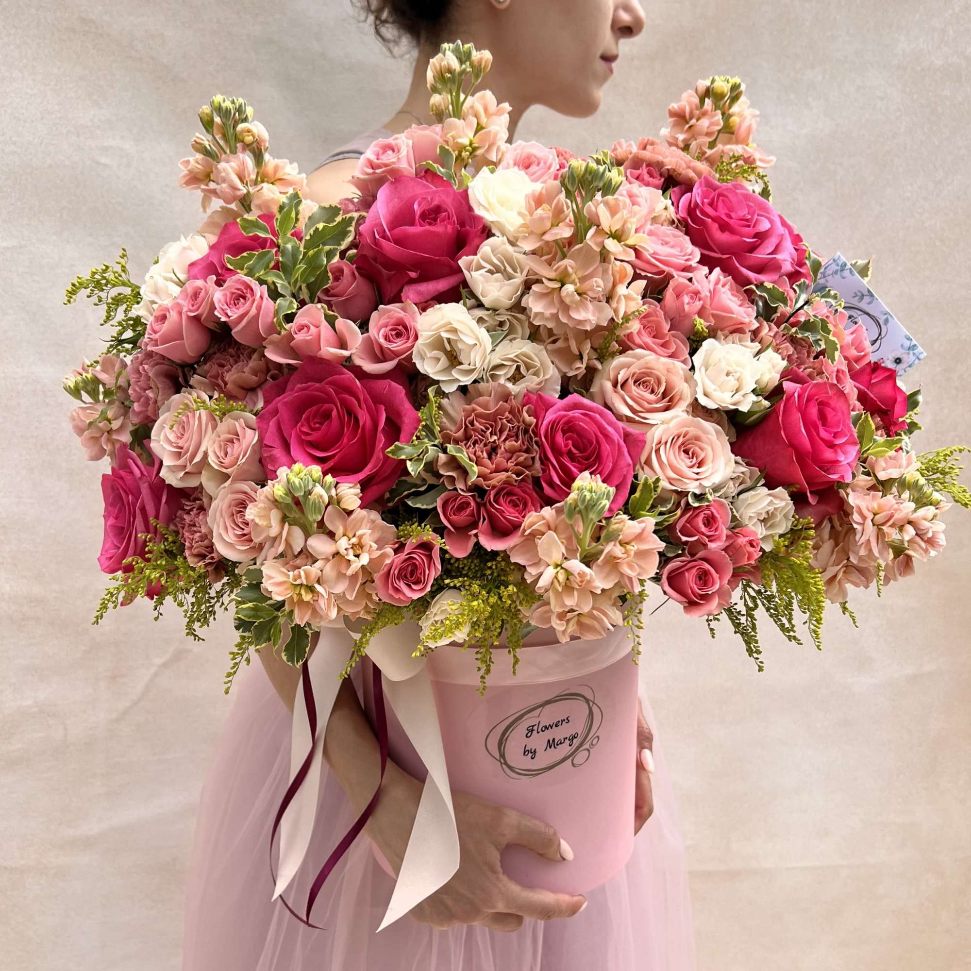 Large pink hatbox arrangement of hot pink and blush roses and mixed flowers held by a woman.