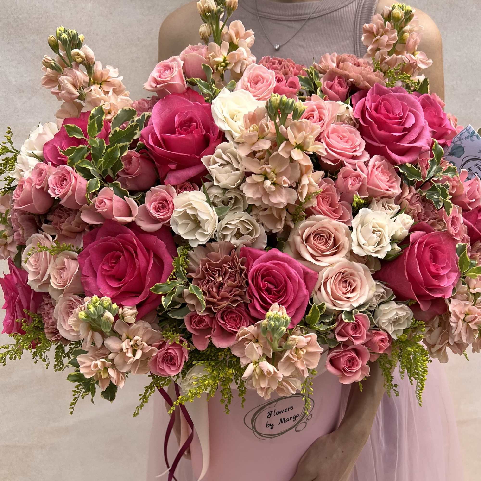 Abundant pink and ivory roses, spray roses, stock, and carnations in a pink hatbox-style container.