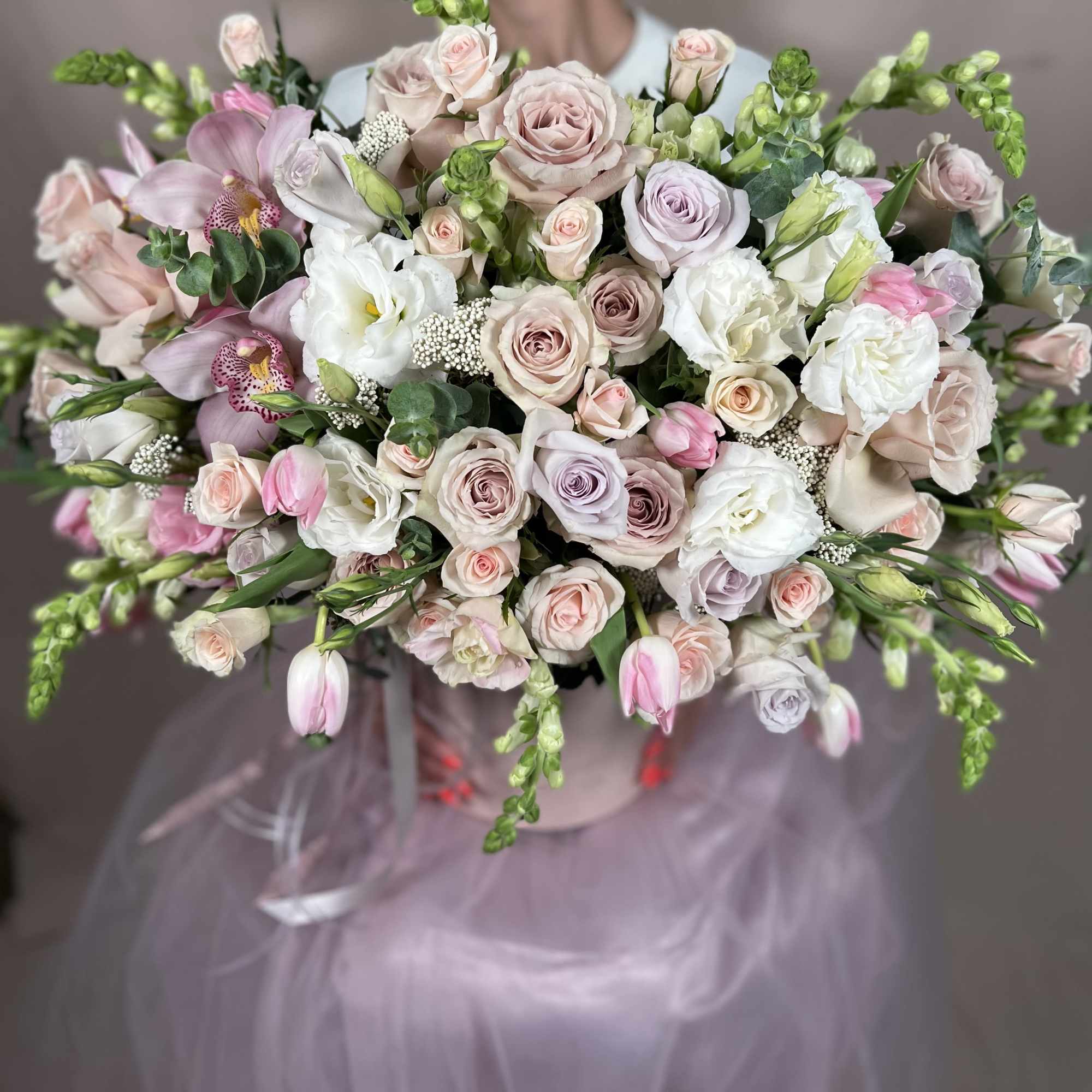 Large pastel arrangement of roses, tulips, orchids, and lisianthus in a round hatbox-style container.