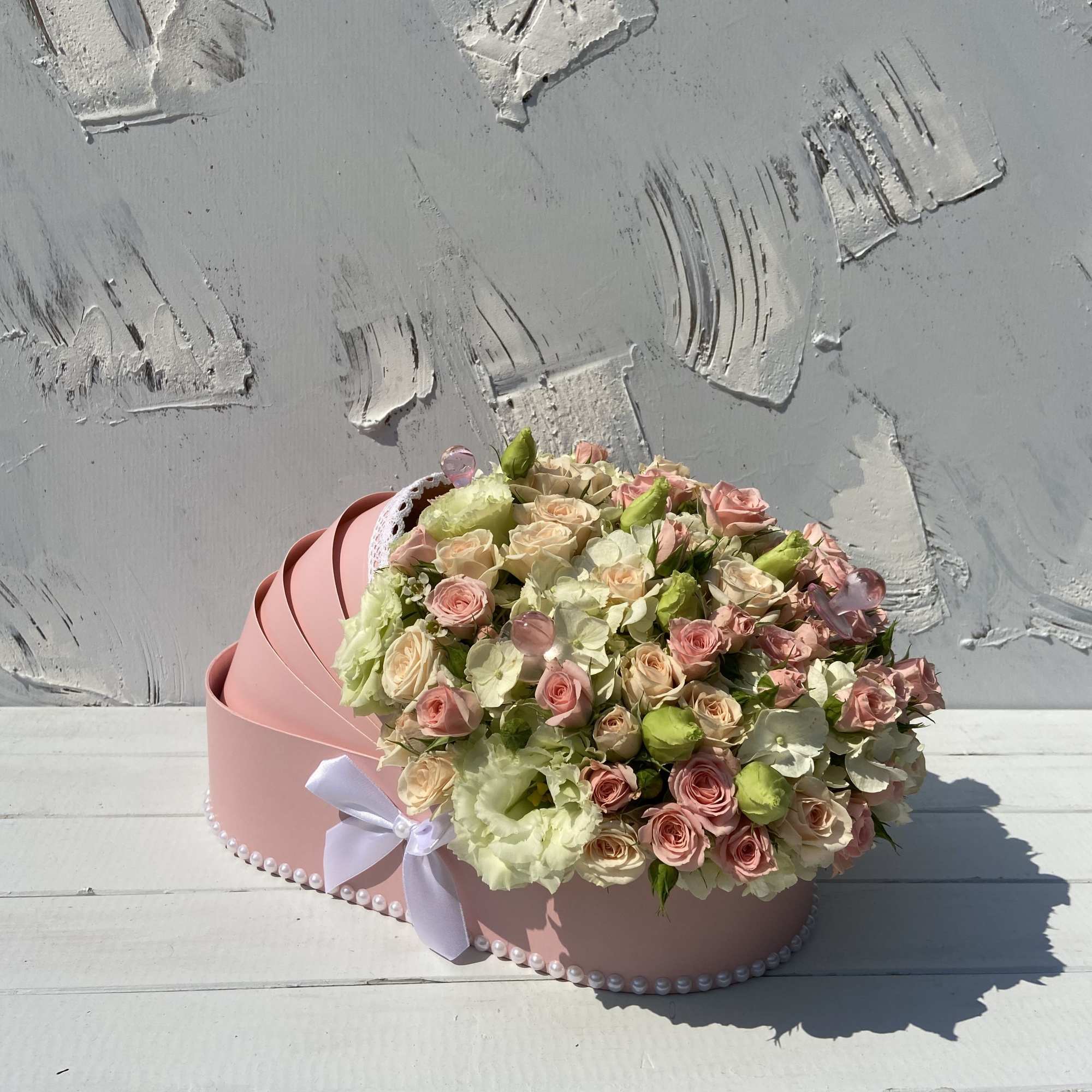 Pastel pink and cream roses arranged in a pink hat-box style container with a white bow.
