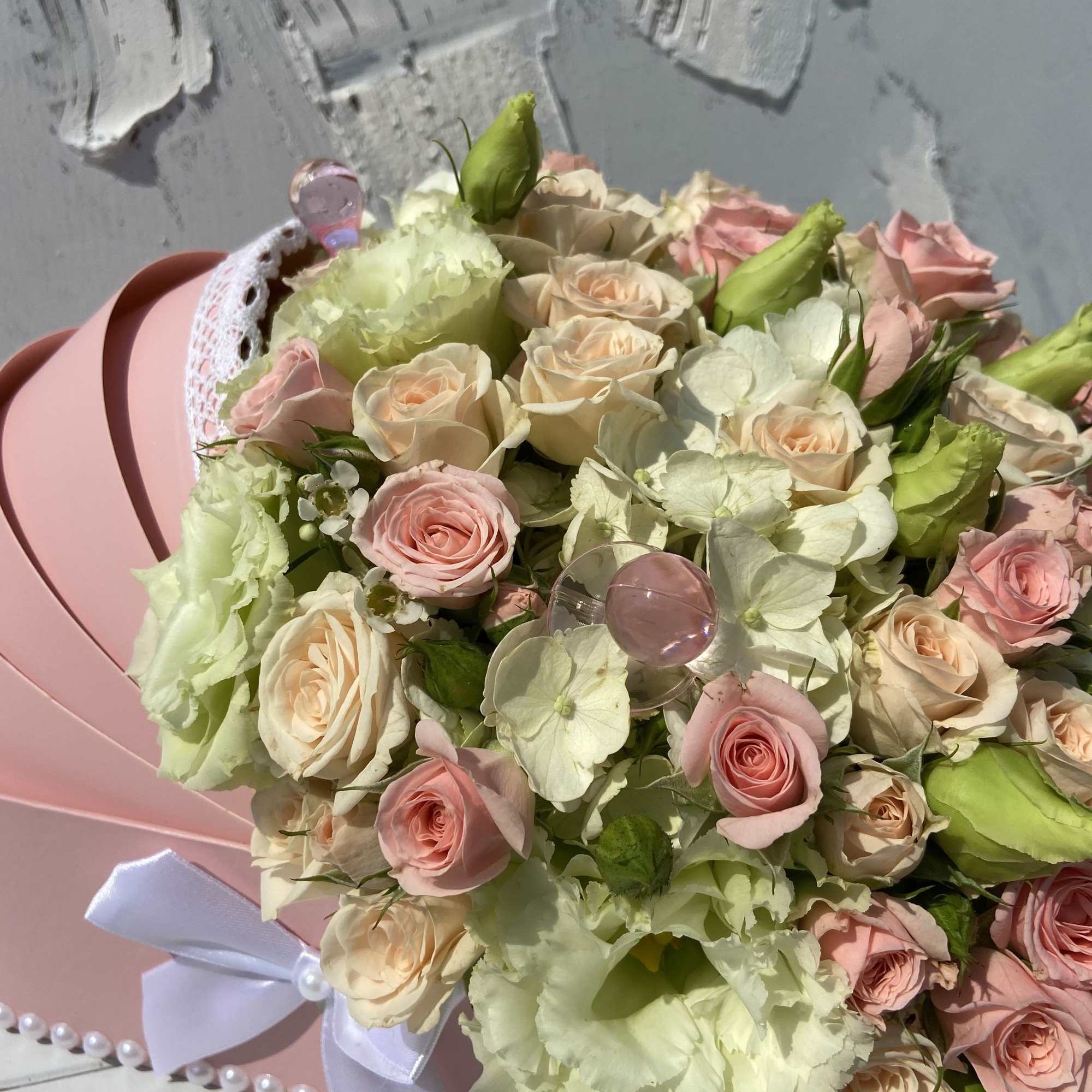 Pastel pink and cream roses with white blooms in a pink hatbox with a white bow.