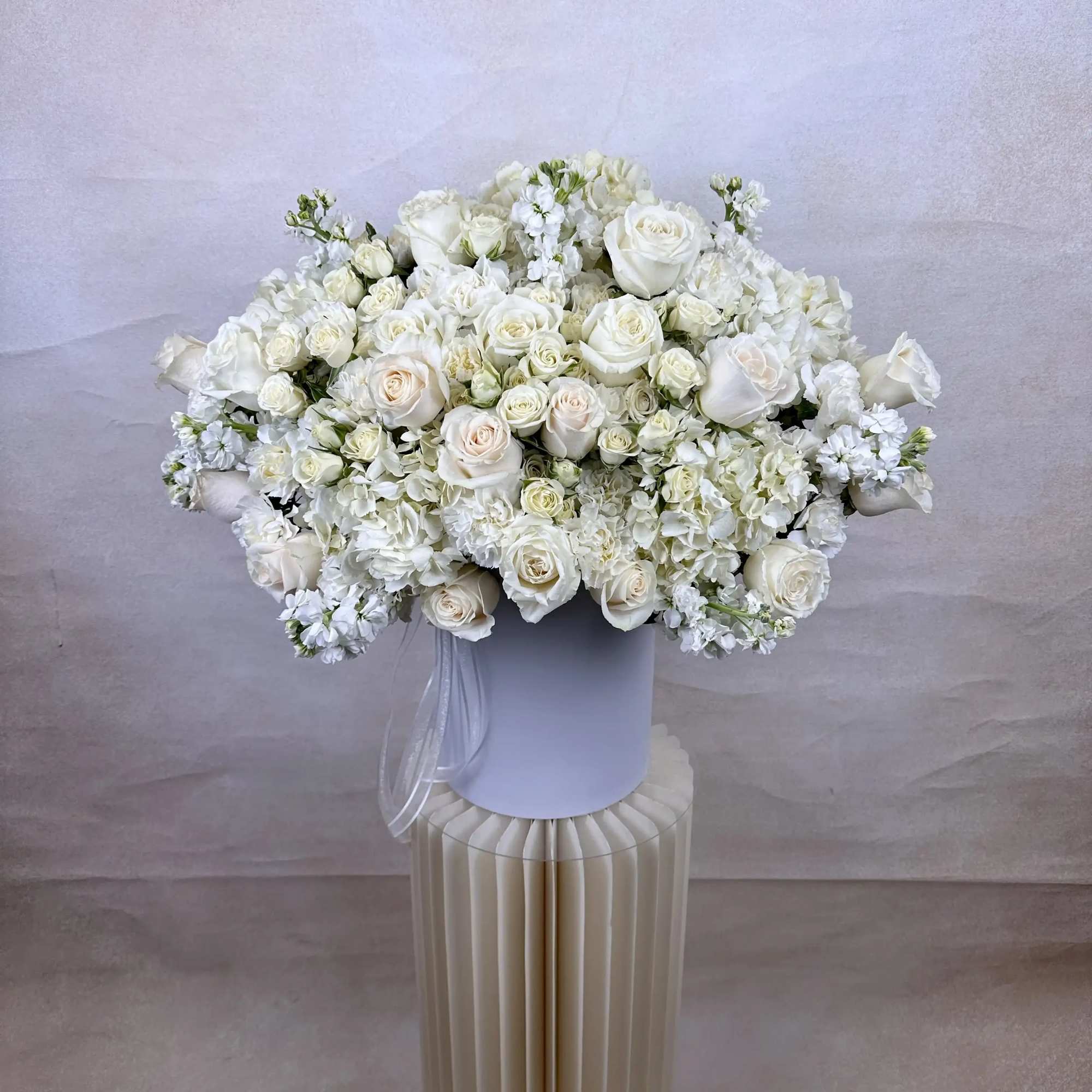 Large all-white arrangement of roses and hydrangeas in a round white box on a pedestal