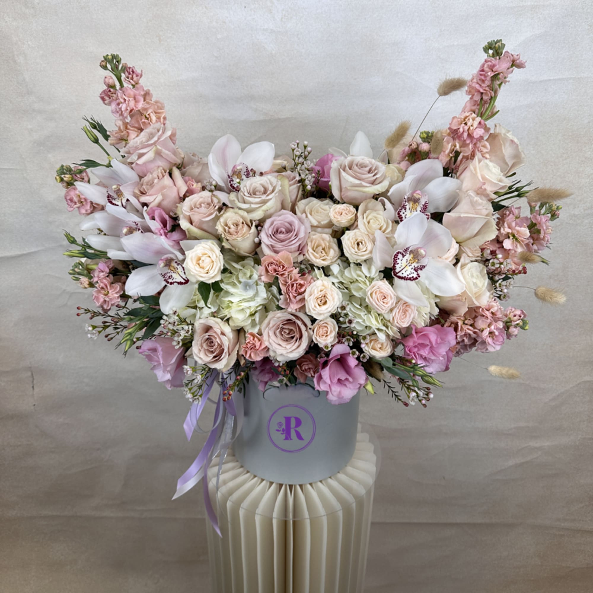 Large pastel pink and ivory flower arrangement with roses, orchids, and hydrangeas in a round hat box.