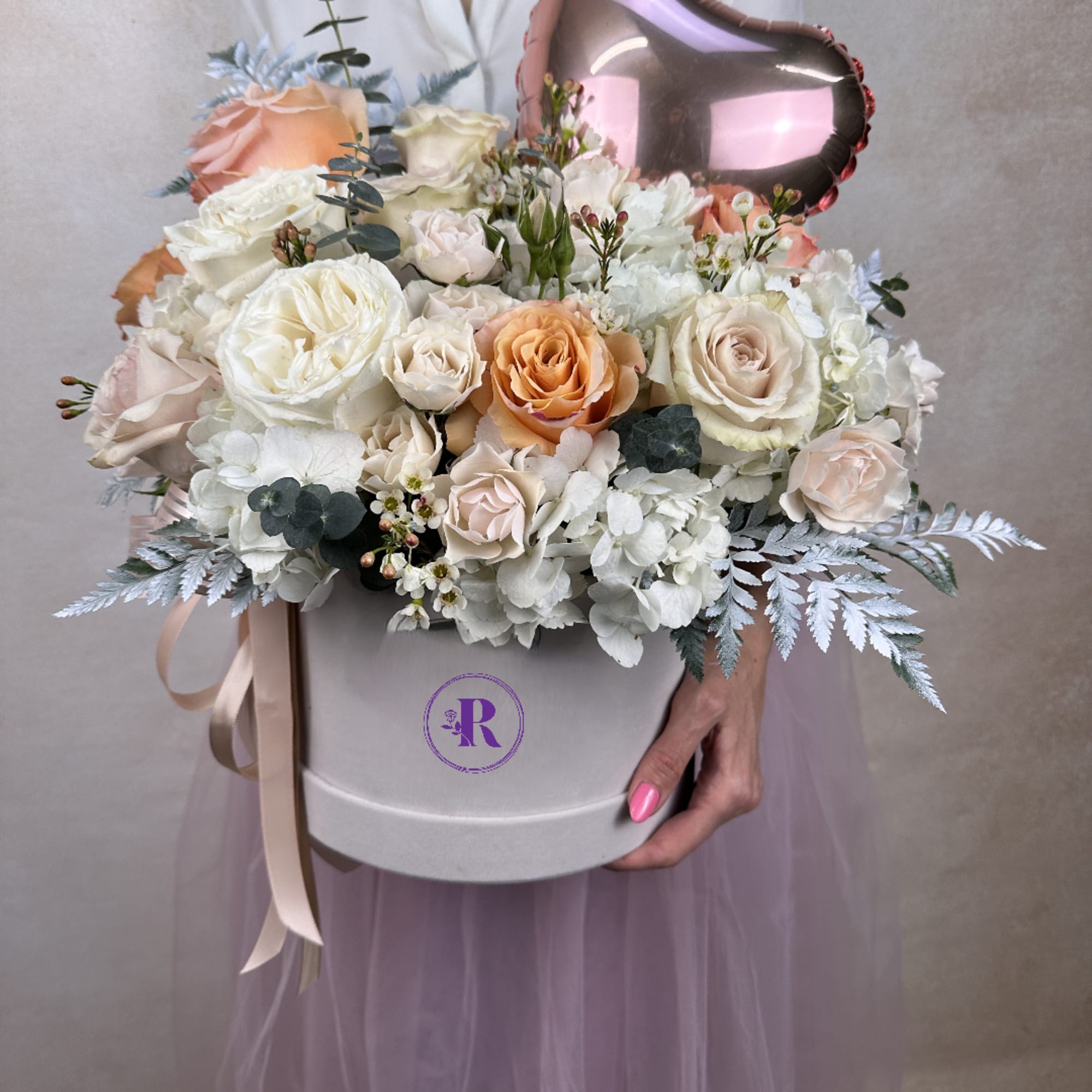 Pastel roses and white hydrangeas in a round hat box with a metallic heart balloon.