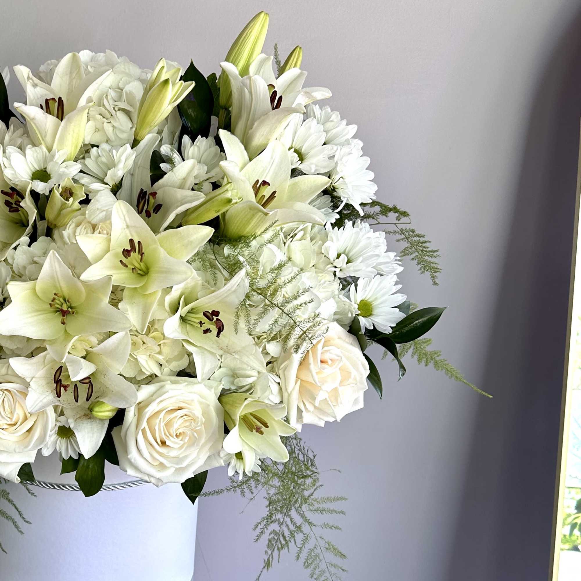 White lilies, roses, and chrysanthemums arranged in a white hatbox-style container