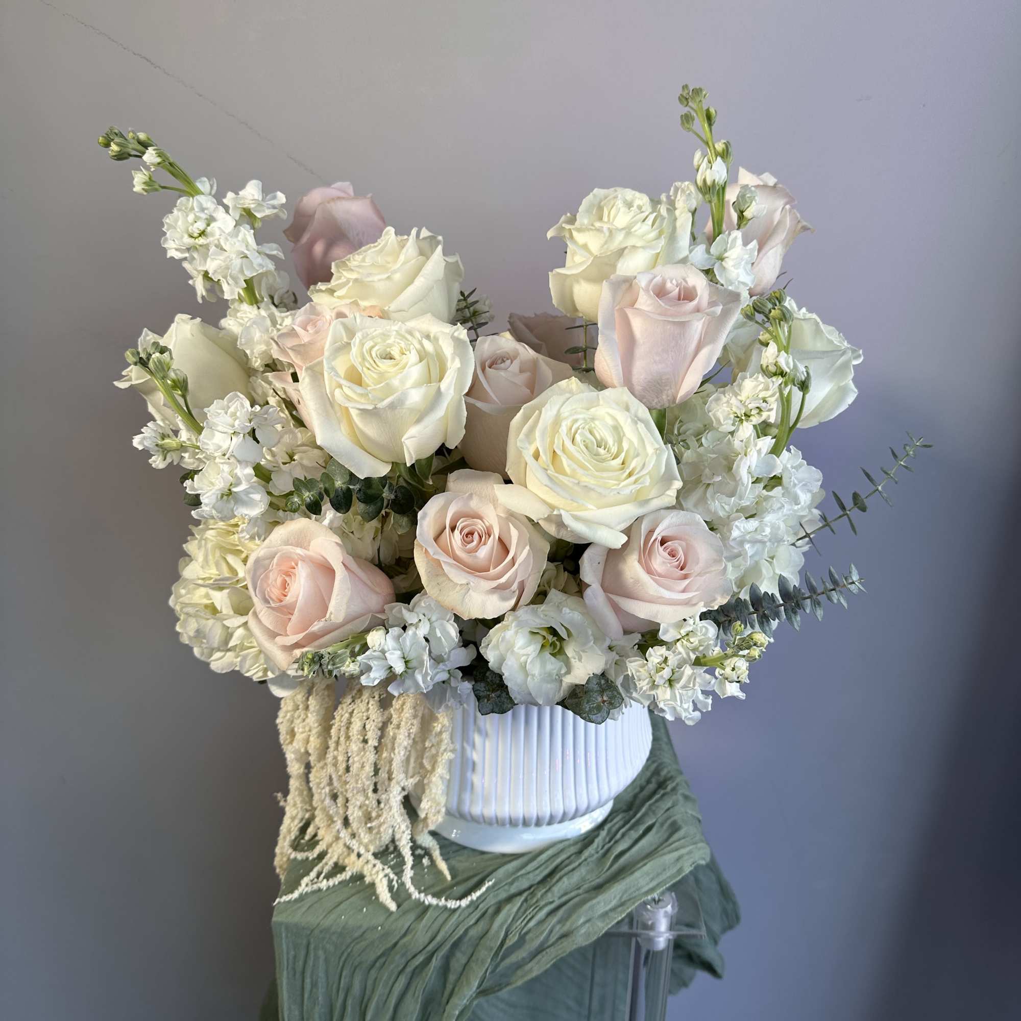 Arrangement of white and blush roses with white accent flowers in a white ceramic vase.
