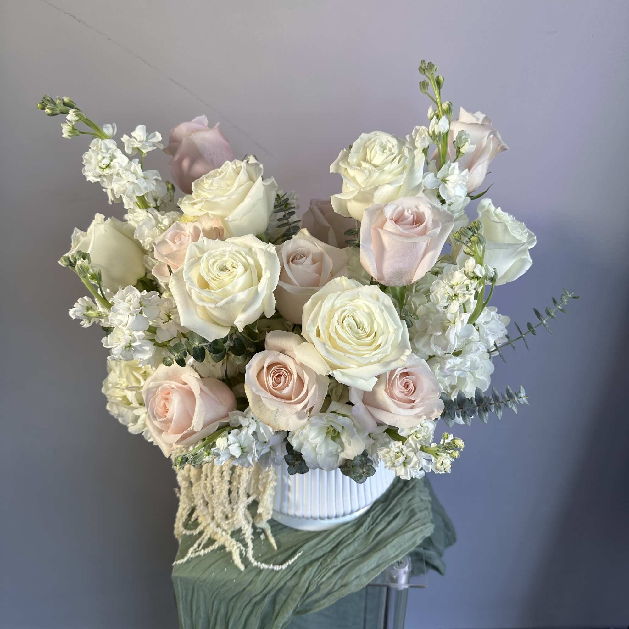 Arrangement of white and blush roses with white accent blooms in a white ribbed vase