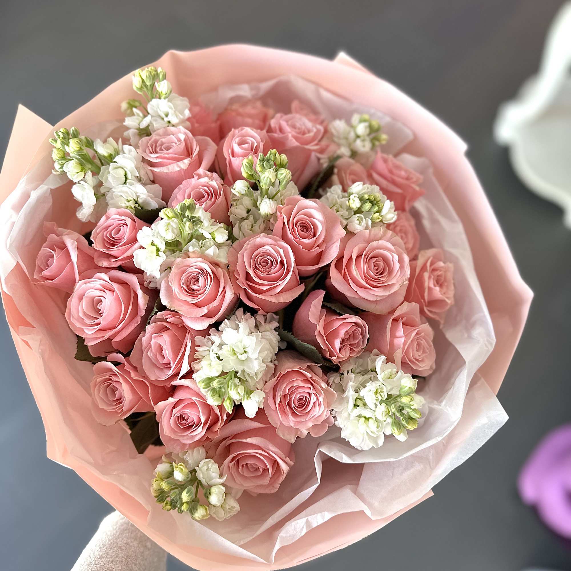 Handheld bouquet of pink roses with white accent flowers wrapped in soft pink paper