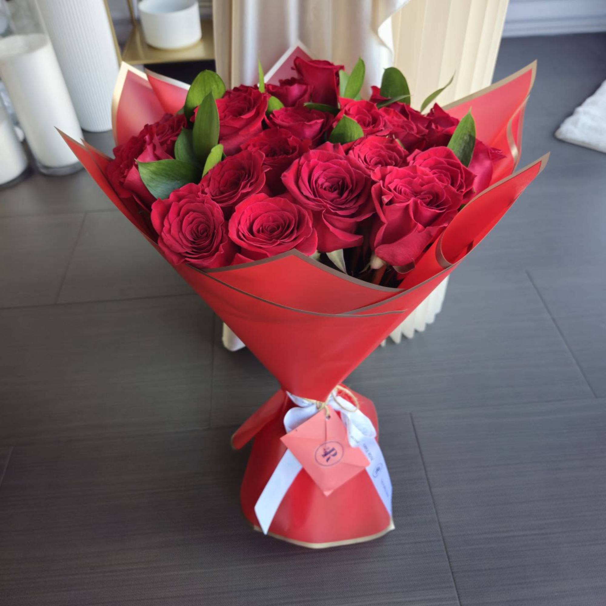 Hand-tied bouquet of red roses wrapped in bright red paper with ribbon and tags