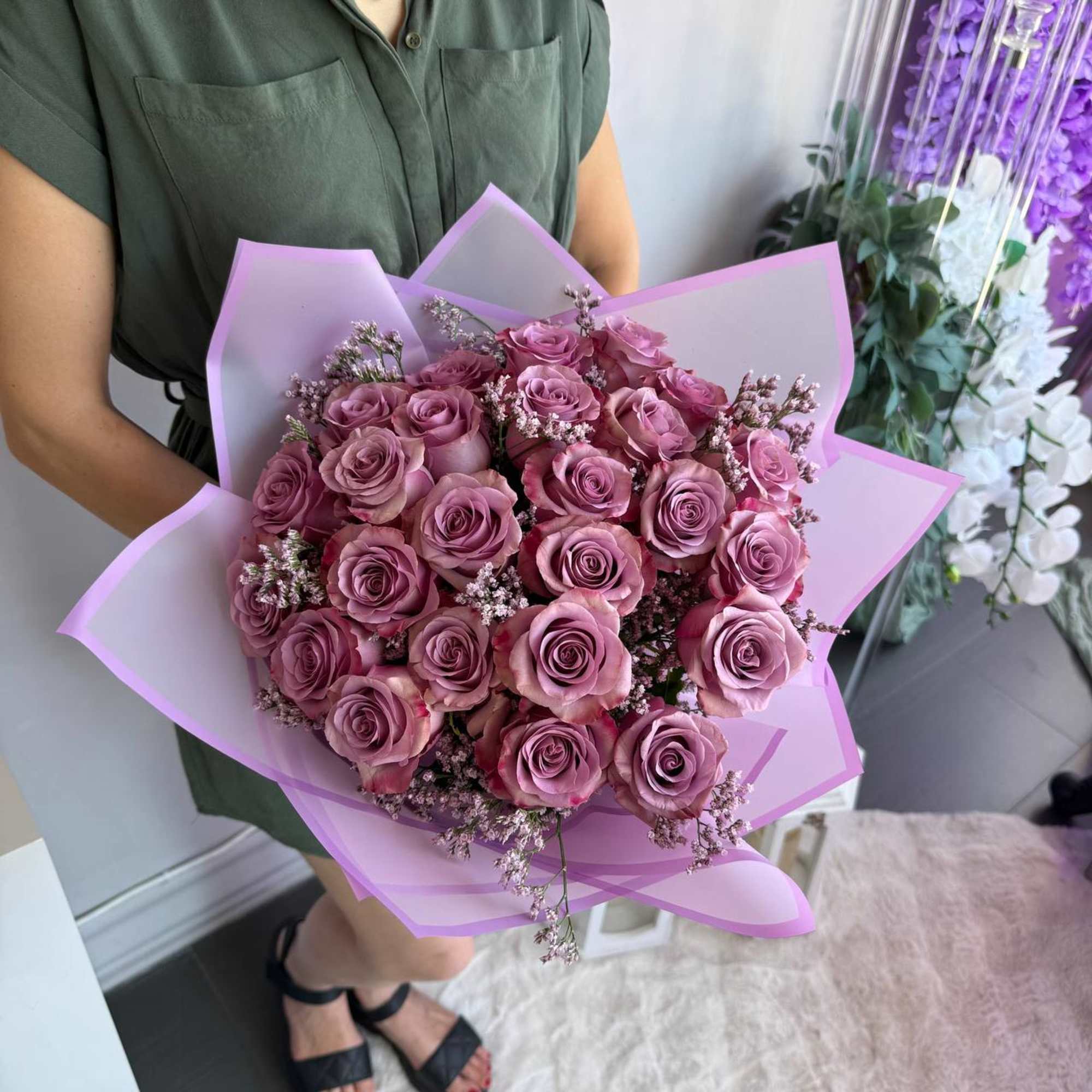 Large bouquet of mauve roses wrapped in pink paper held by a person in a green dress