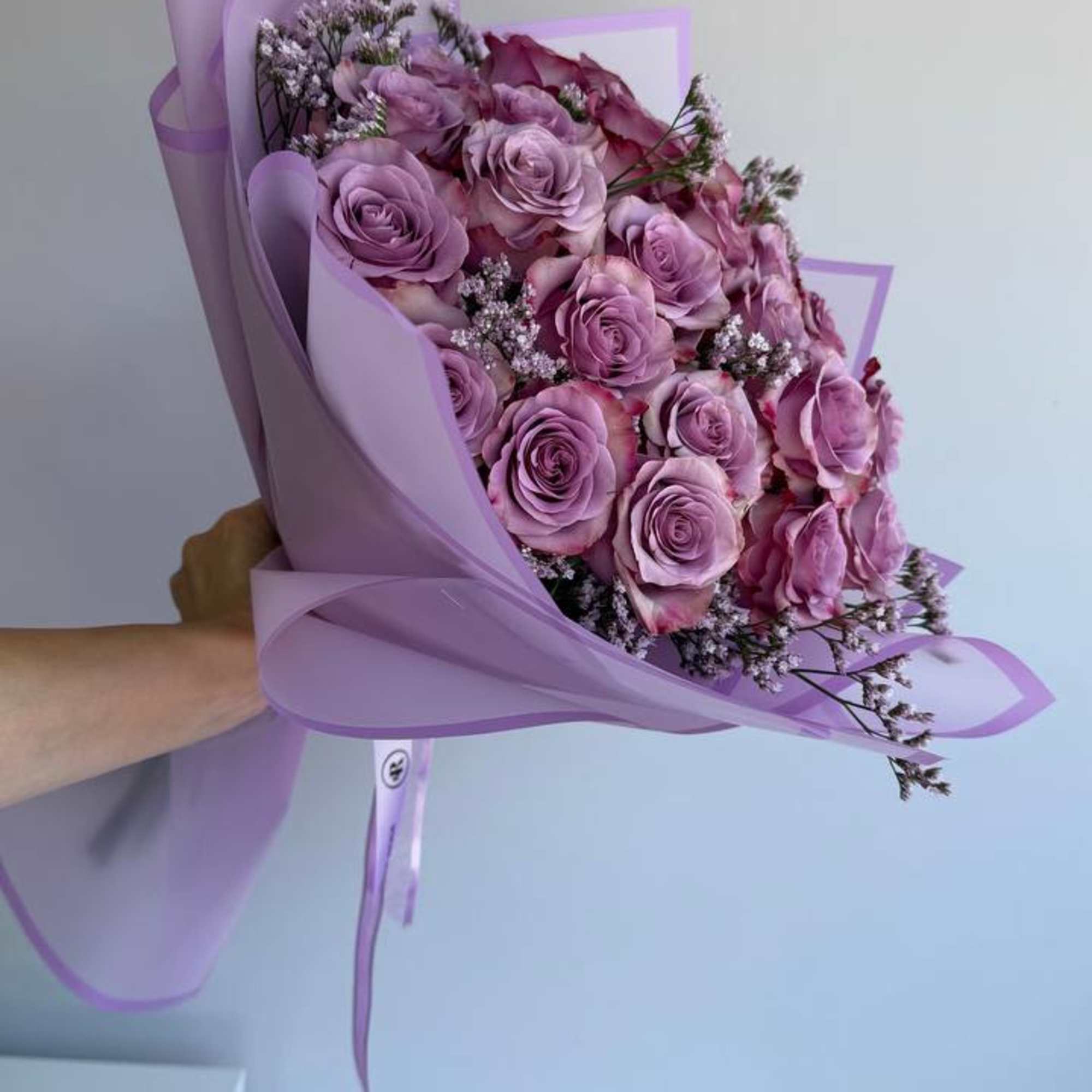 Large bouquet of lavender roses wrapped in layered purple paper and tied with ribbon