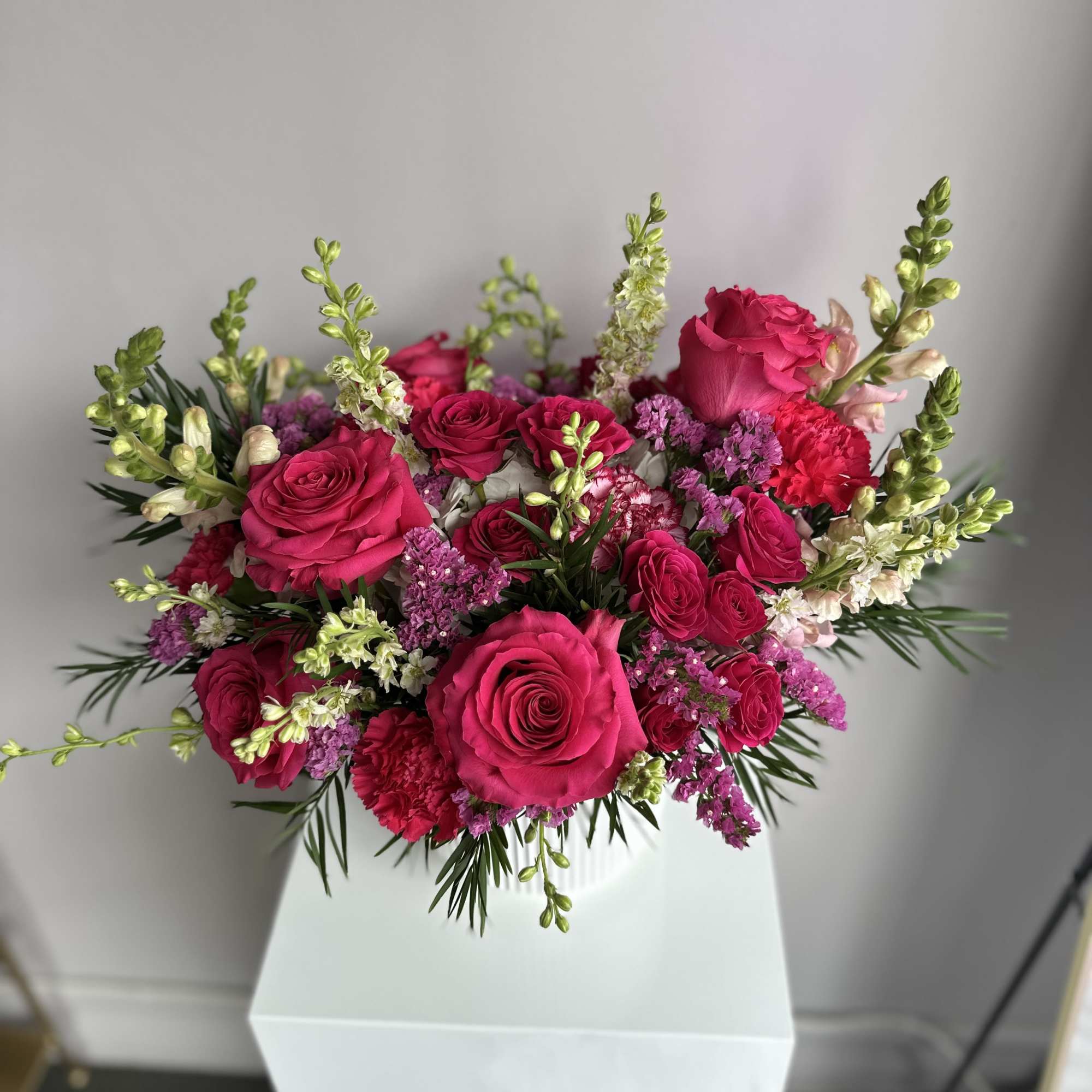 Low arrangement of bright pink roses, carnations, and snapdragons in a white ceramic vase