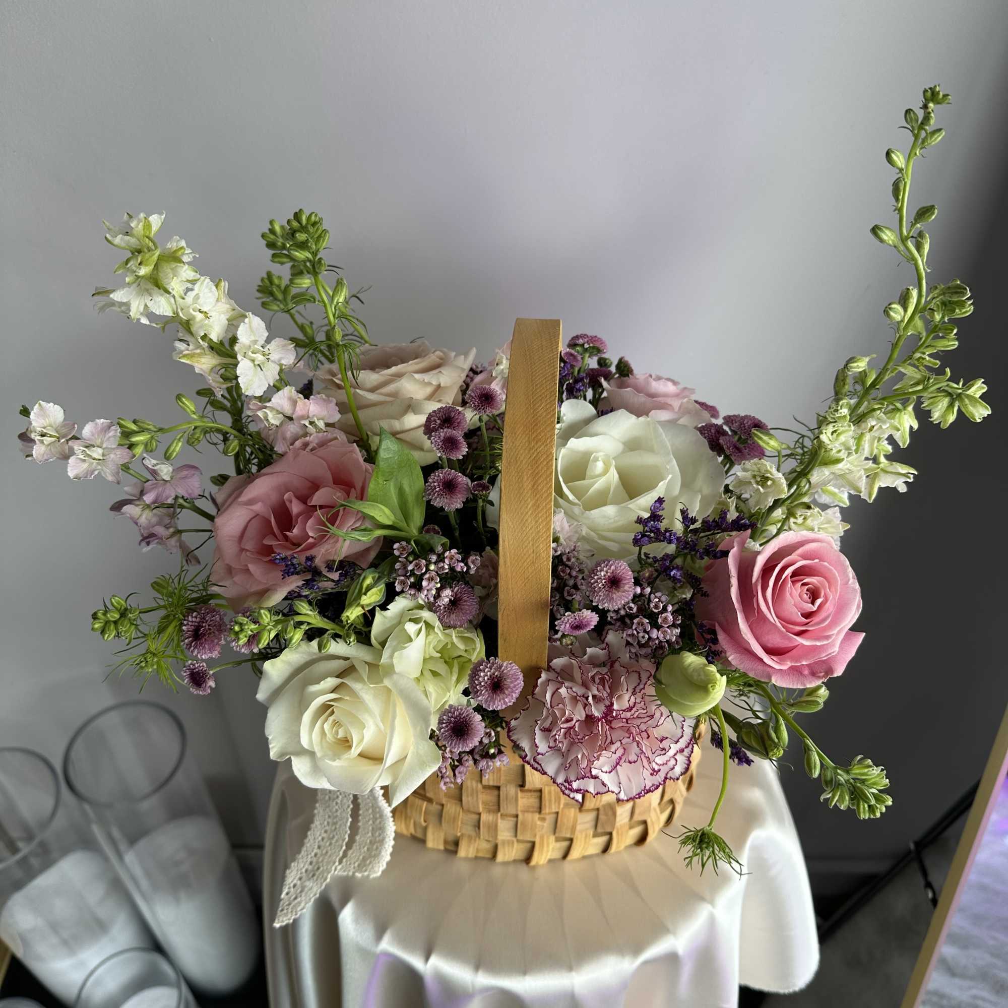 Basket arrangement of pink and white roses, carnations, and purple mums on a small draped round table