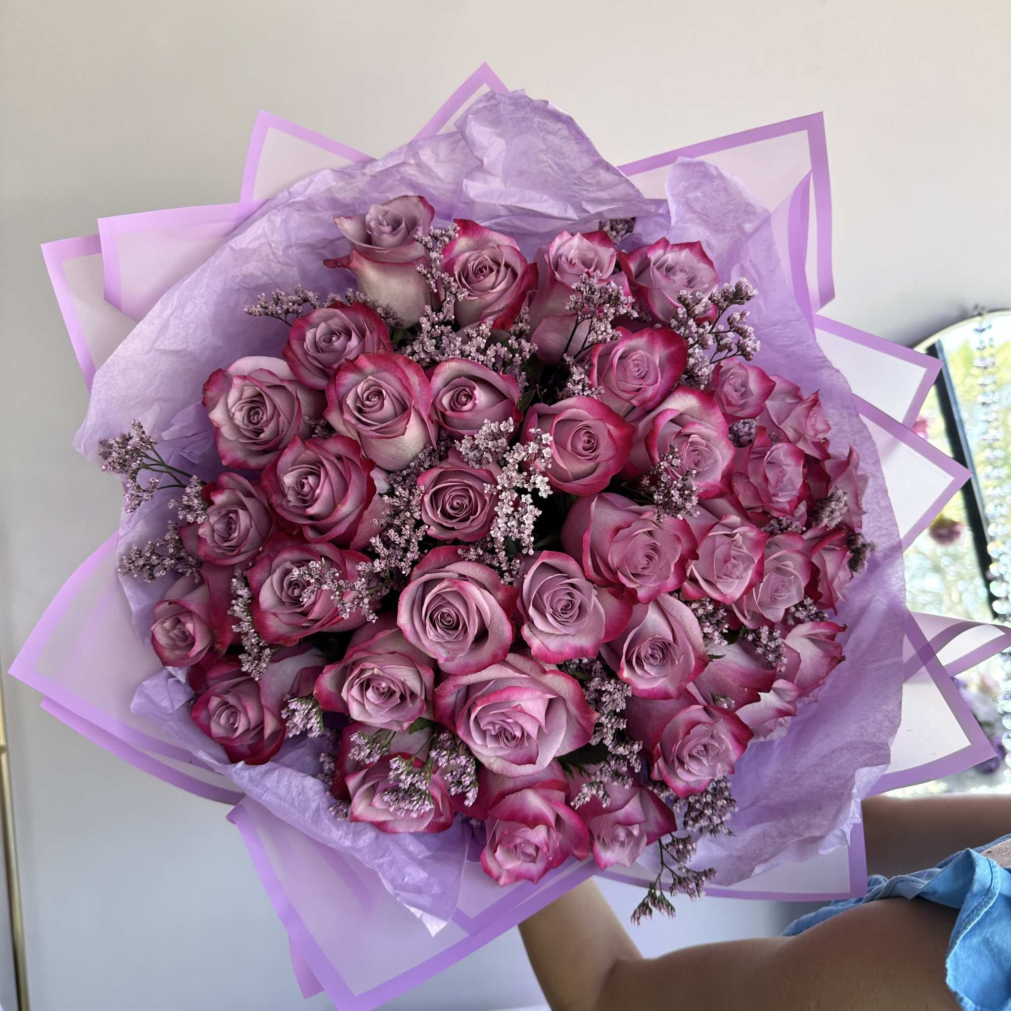 Large bouquet of pink and lavender roses wrapped in lilac and pink paper.