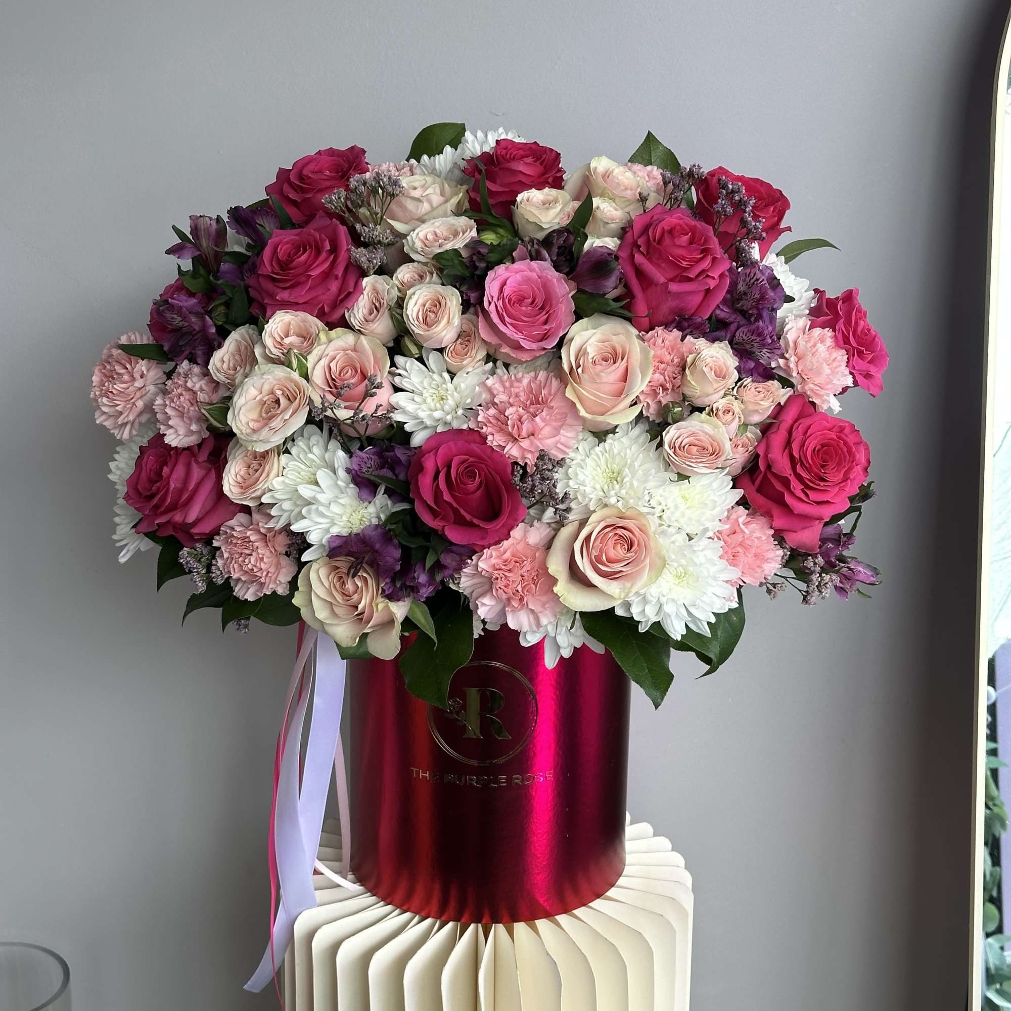 Pink and cream rose arrangement with white mums in a red hatbox-style container