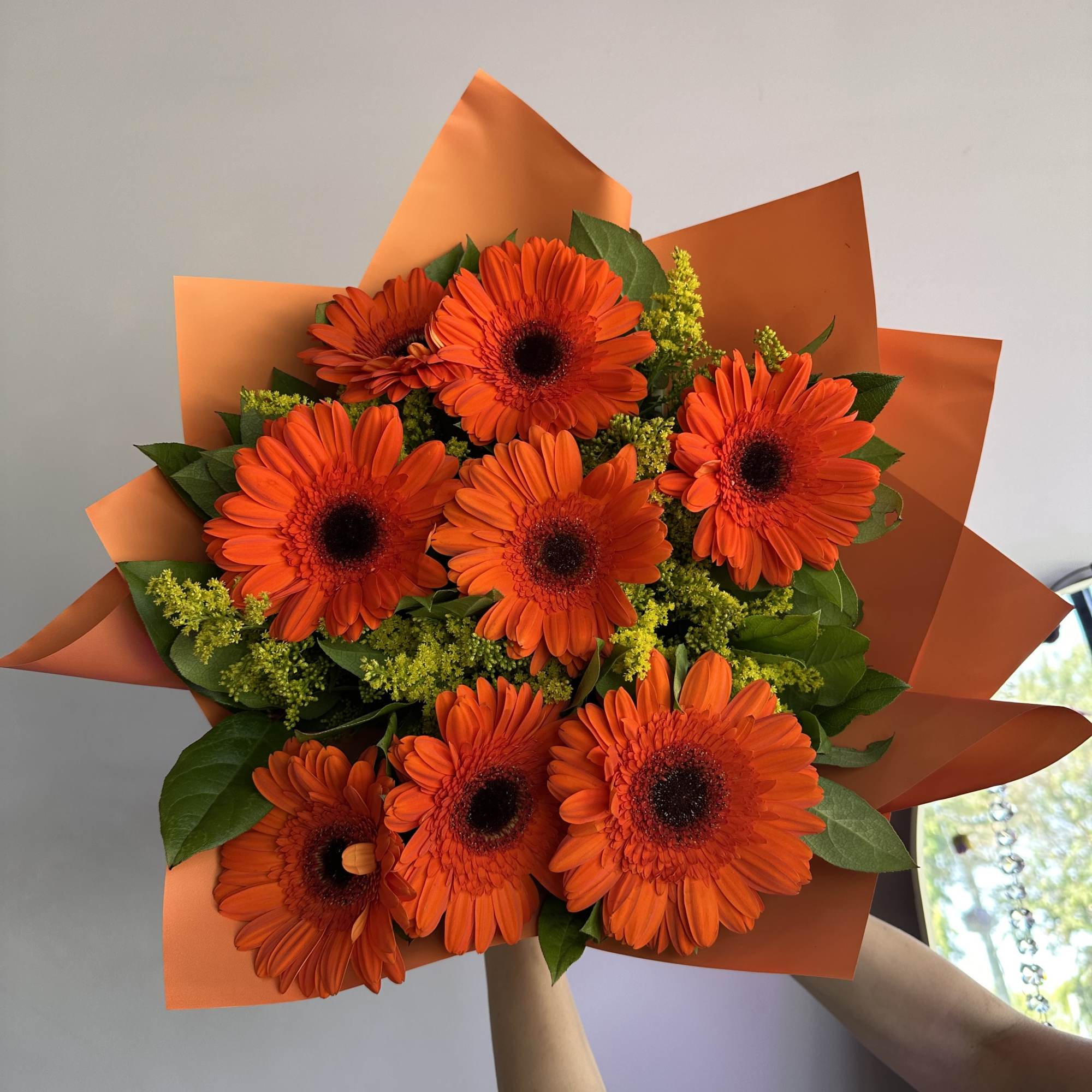 Bouquet of bright orange gerbera daisies with yellow filler wrapped in orange paper