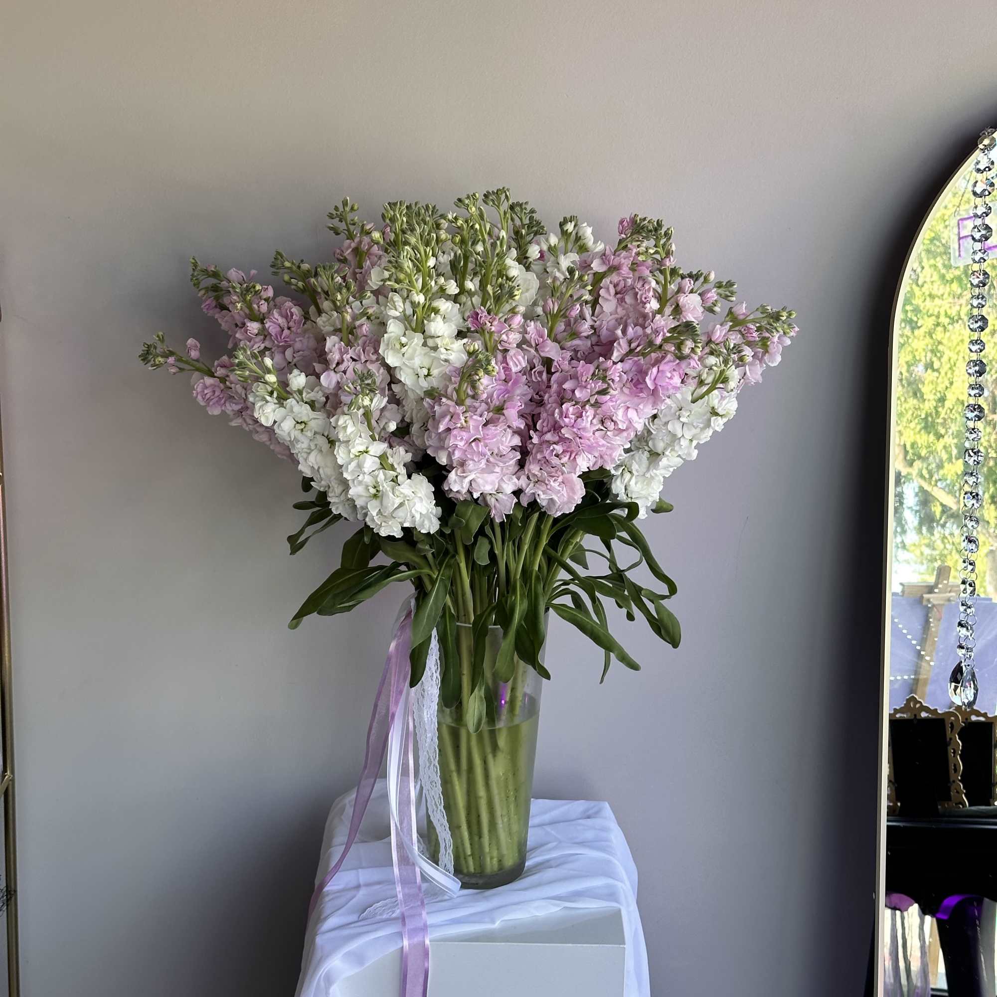 Tall arrangement of pink and white stock flowers in a clear glass vase with ribbons.