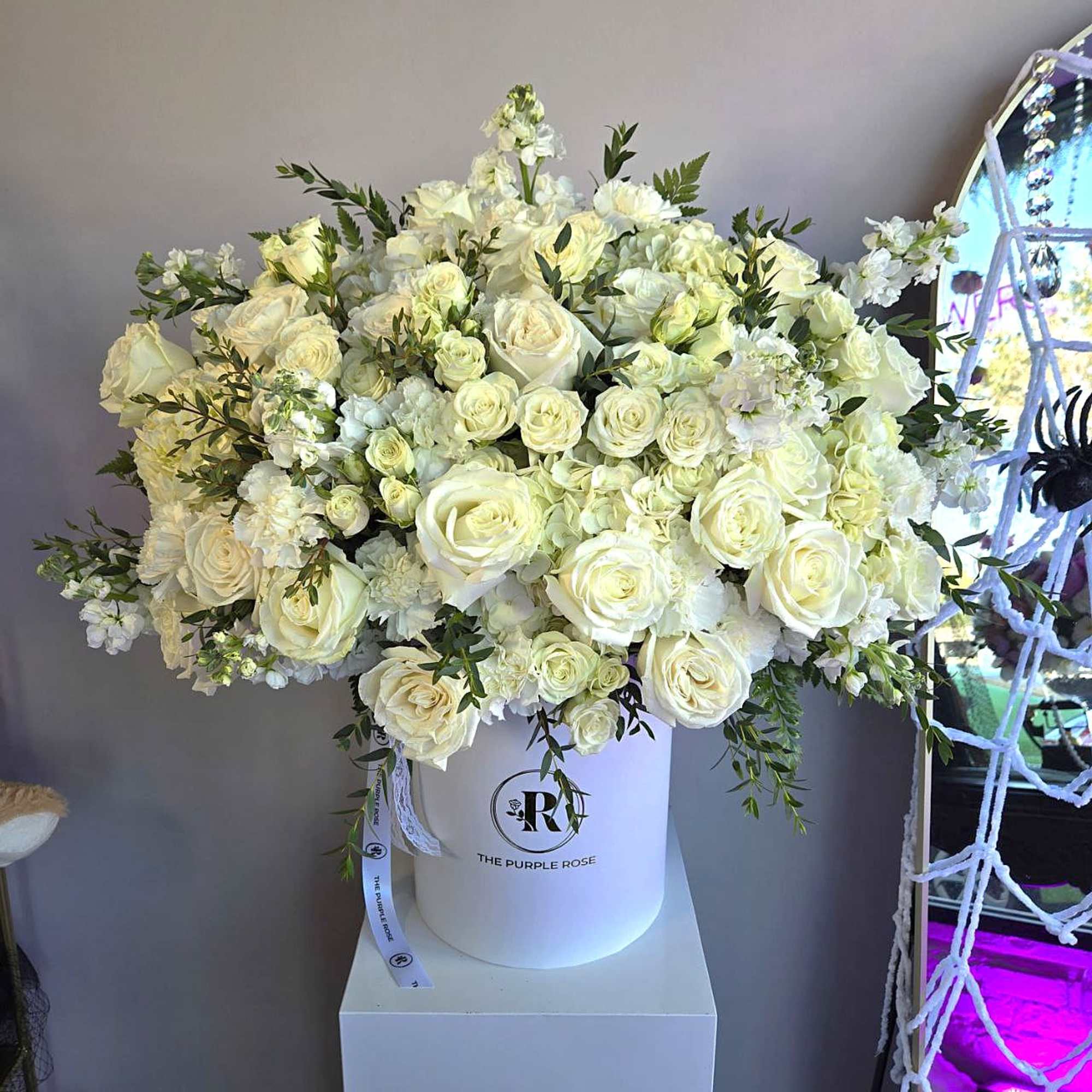 Large white hatbox filled with abundant ivory roses, hydrangeas, carnations, and other white blooms