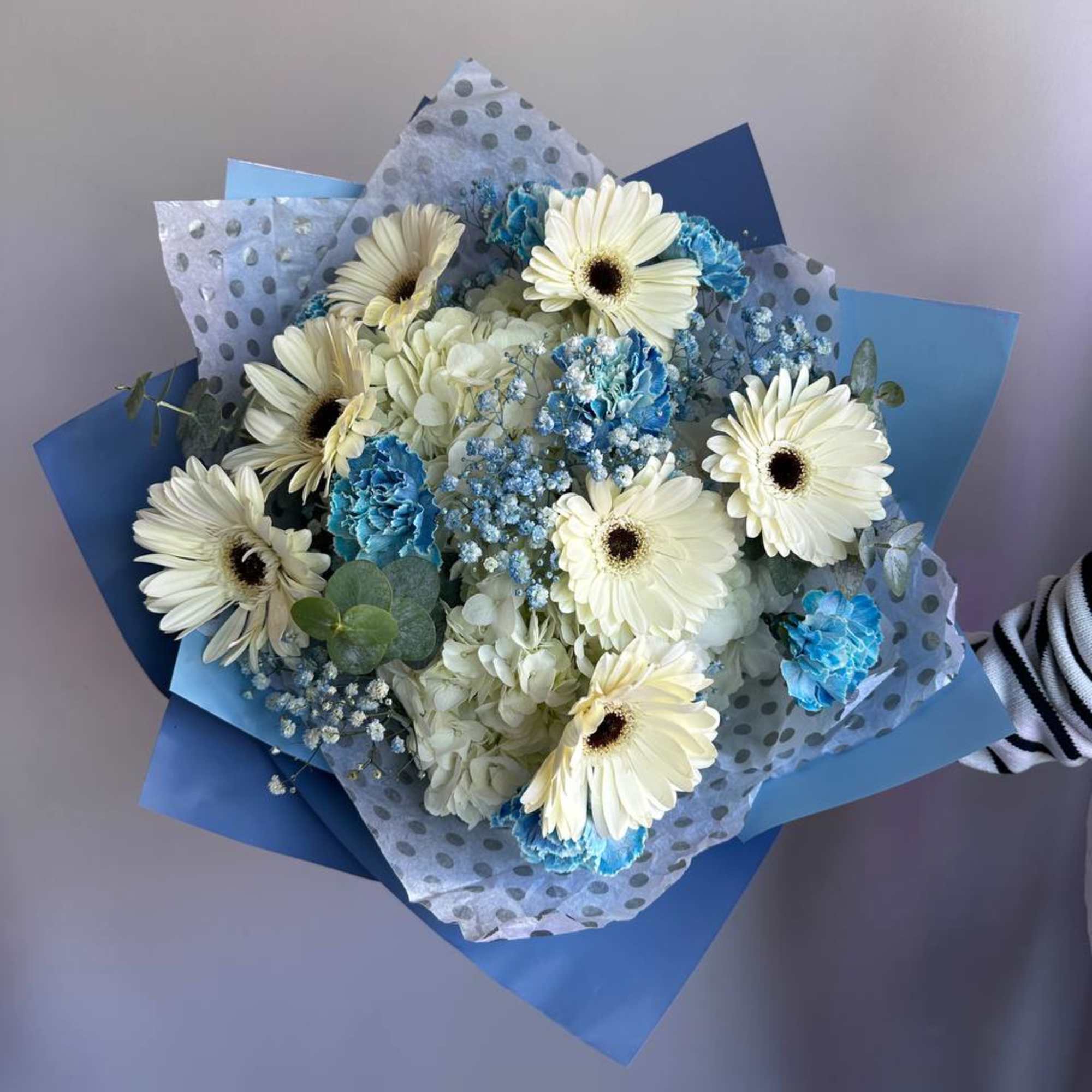 Hand-tied bouquet of white gerbera daisies and blue flowers wrapped in blue and polka dot paper