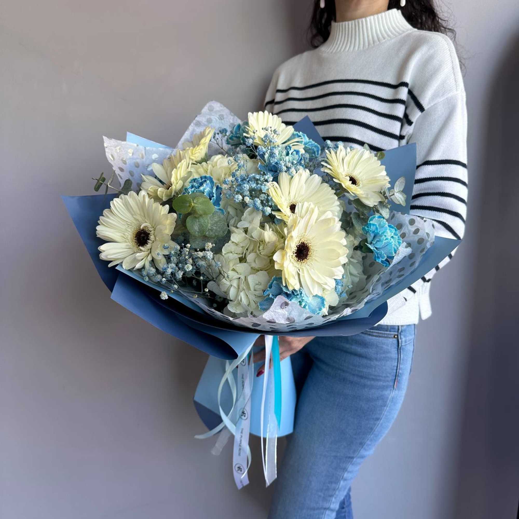 Large bouquet of cream gerbera daisies with blue flowers wrapped in blue and polka-dot paper
