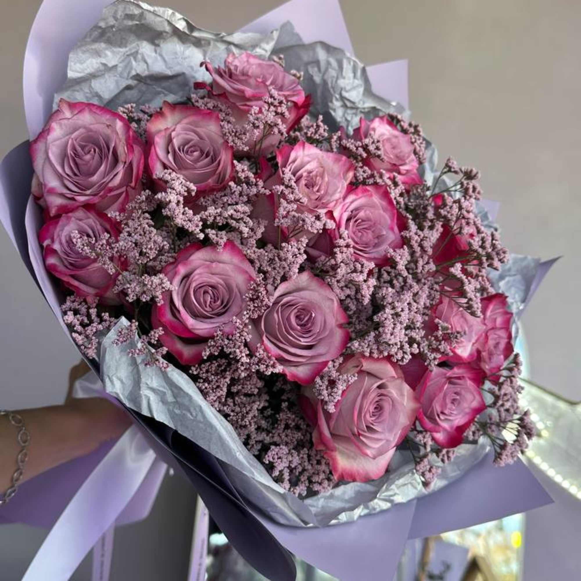 Hand-tied bouquet of pink-lavender roses with matching filler flowers wrapped in lilac and silver paper.