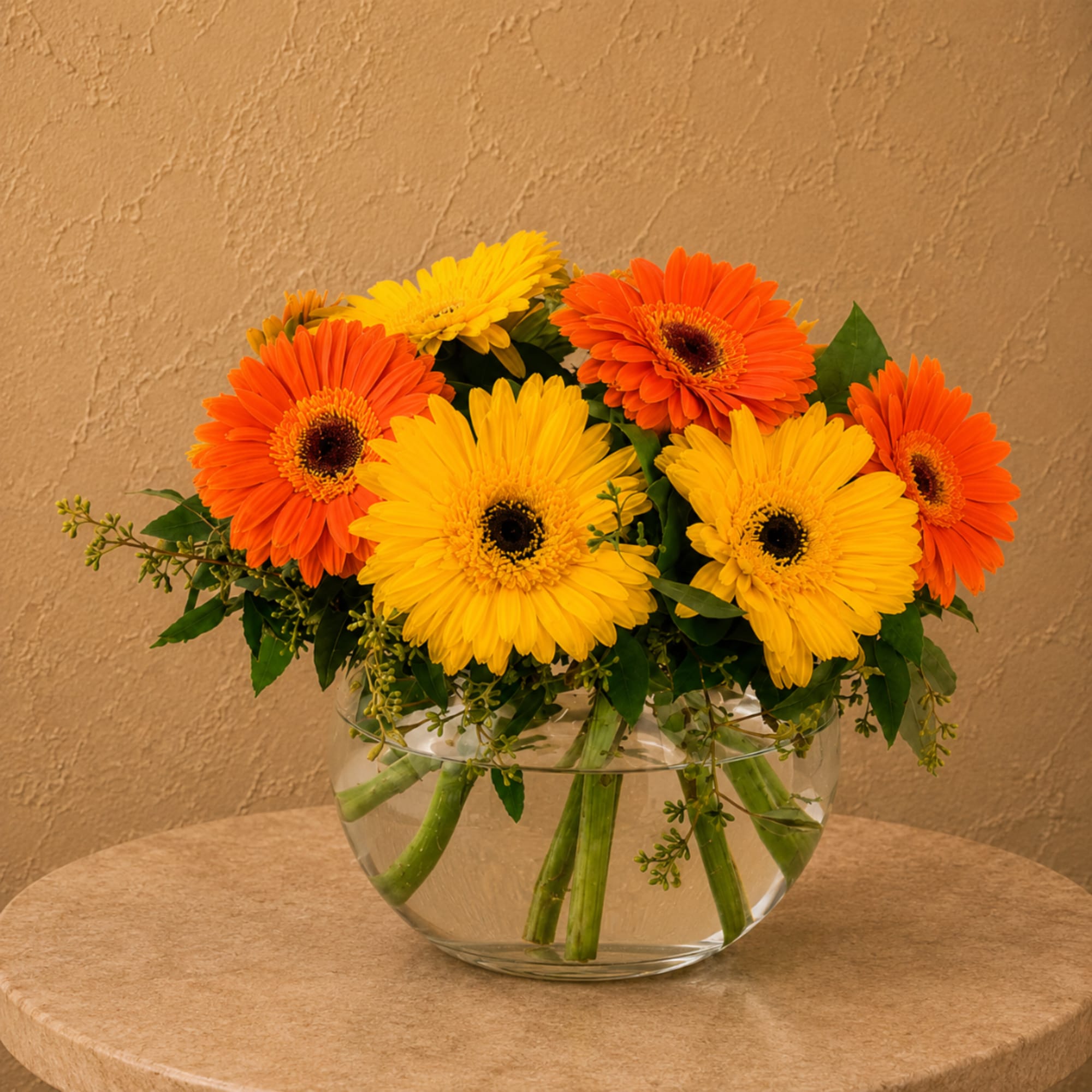 Orange and yellow gerbera daisies in a clear glass bowl vase