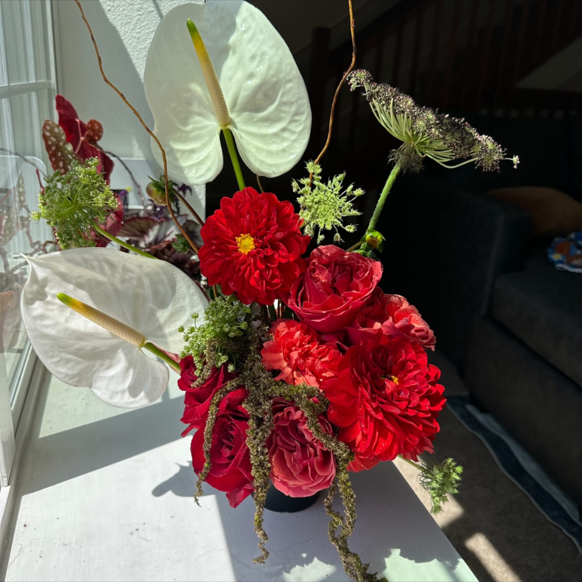 Red floral arrangement with white anthuriums in a black vase