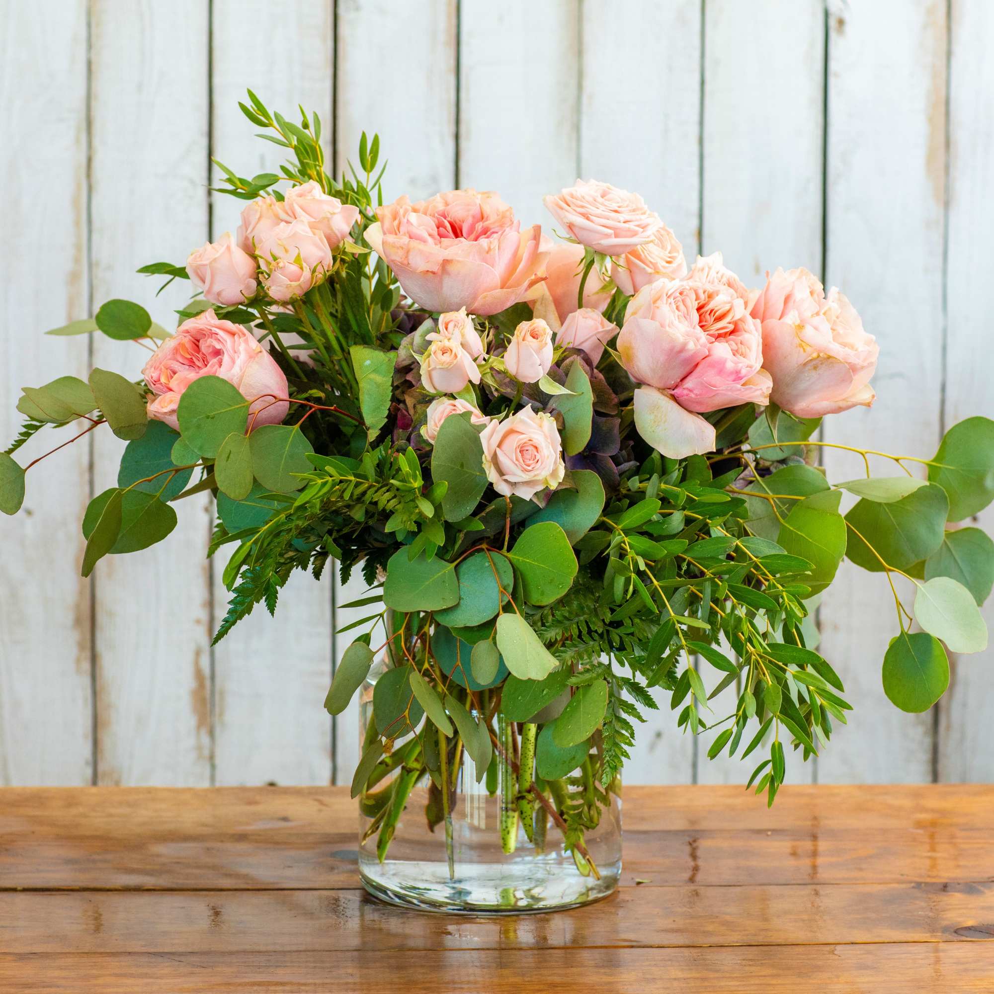 Pink roses in a clear glass vase with eucalyptus