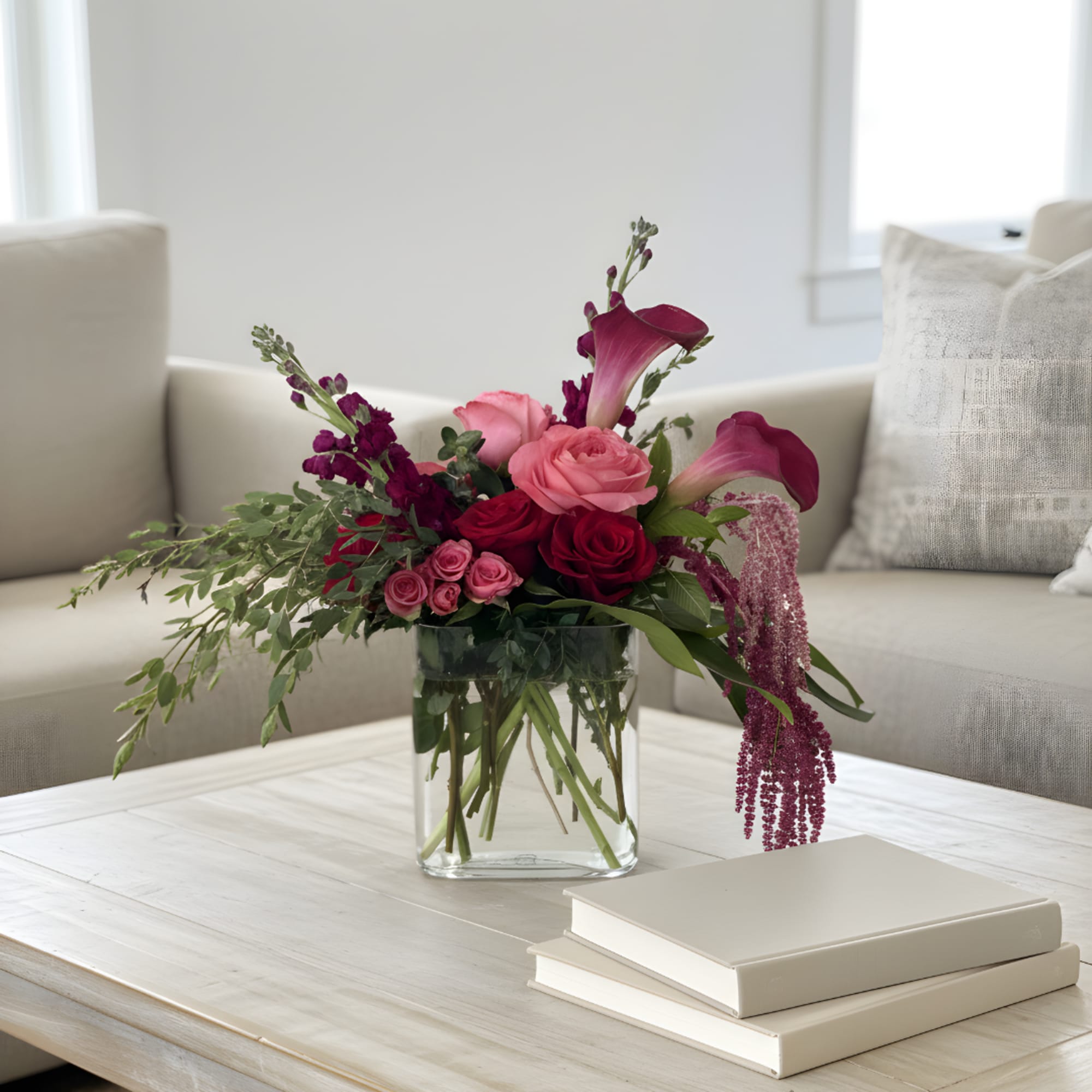 Pink and burgundy floral arrangement in a clear glass vase on a coffee table