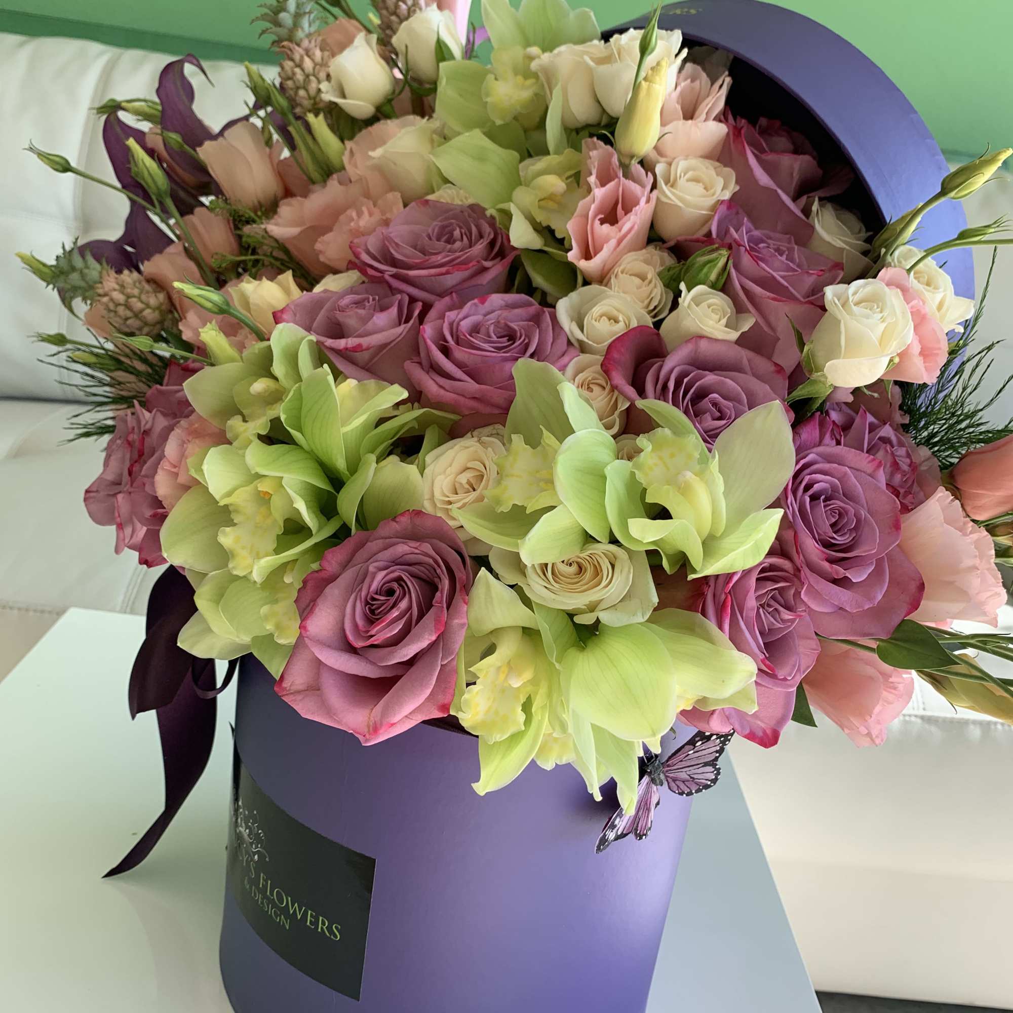 Bouquet of pink and lavender roses with green orchids in a purple hatbox