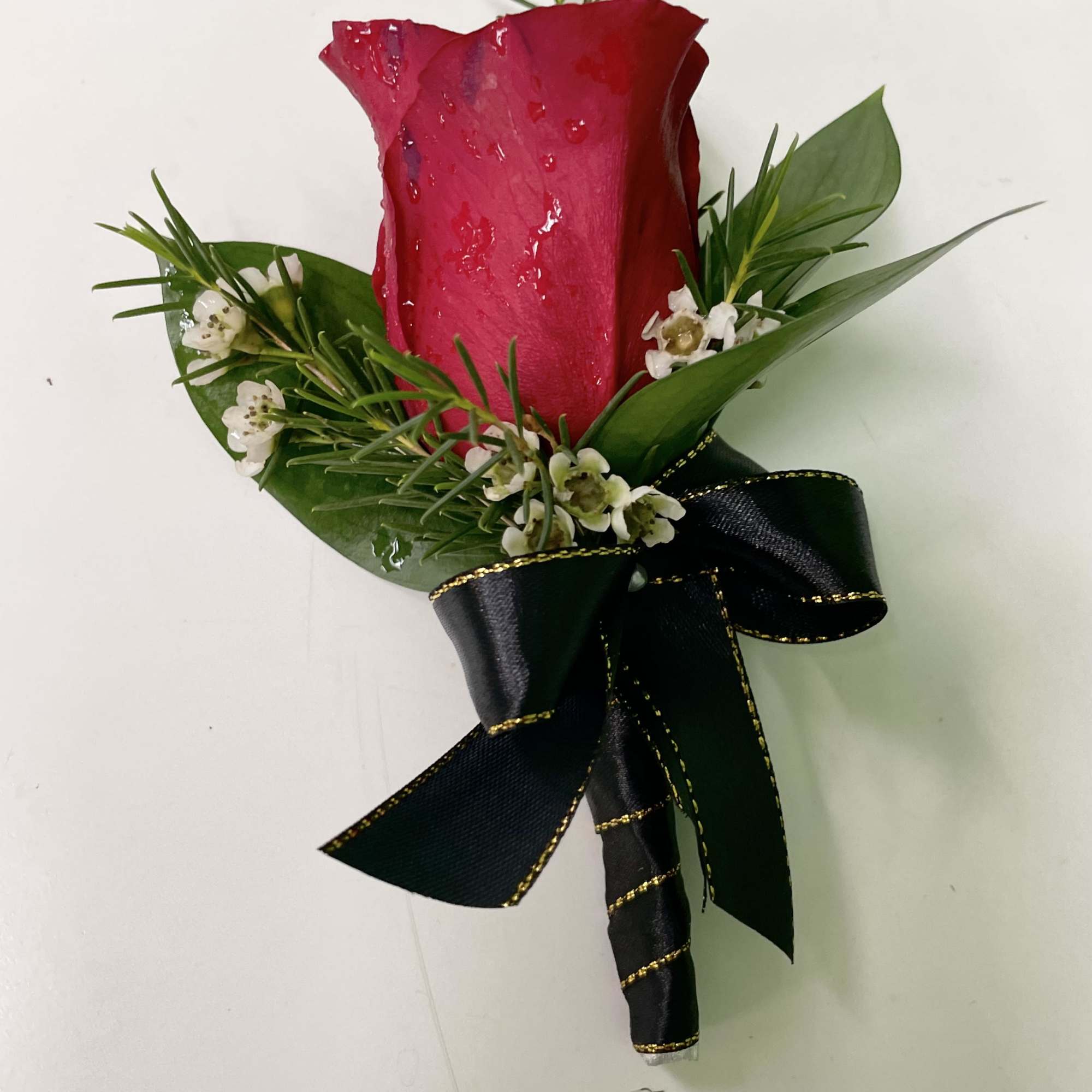 Single red rose boutonniere with small white flowers and a black ribbon