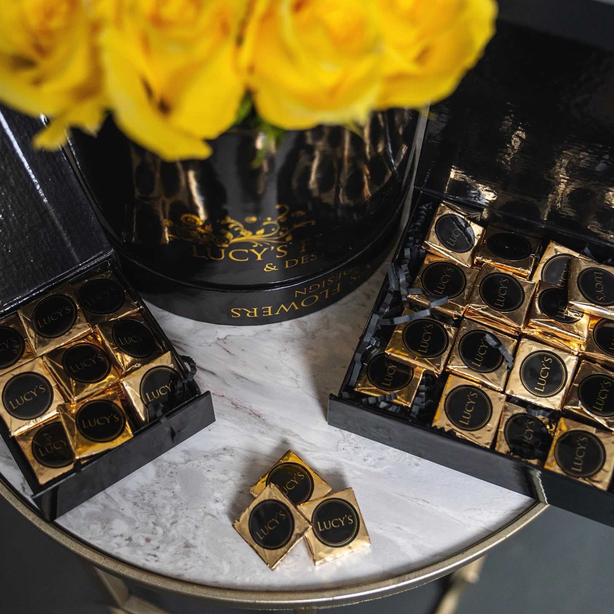 Yellow roses in a black gift box with gold-wrapped chocolates