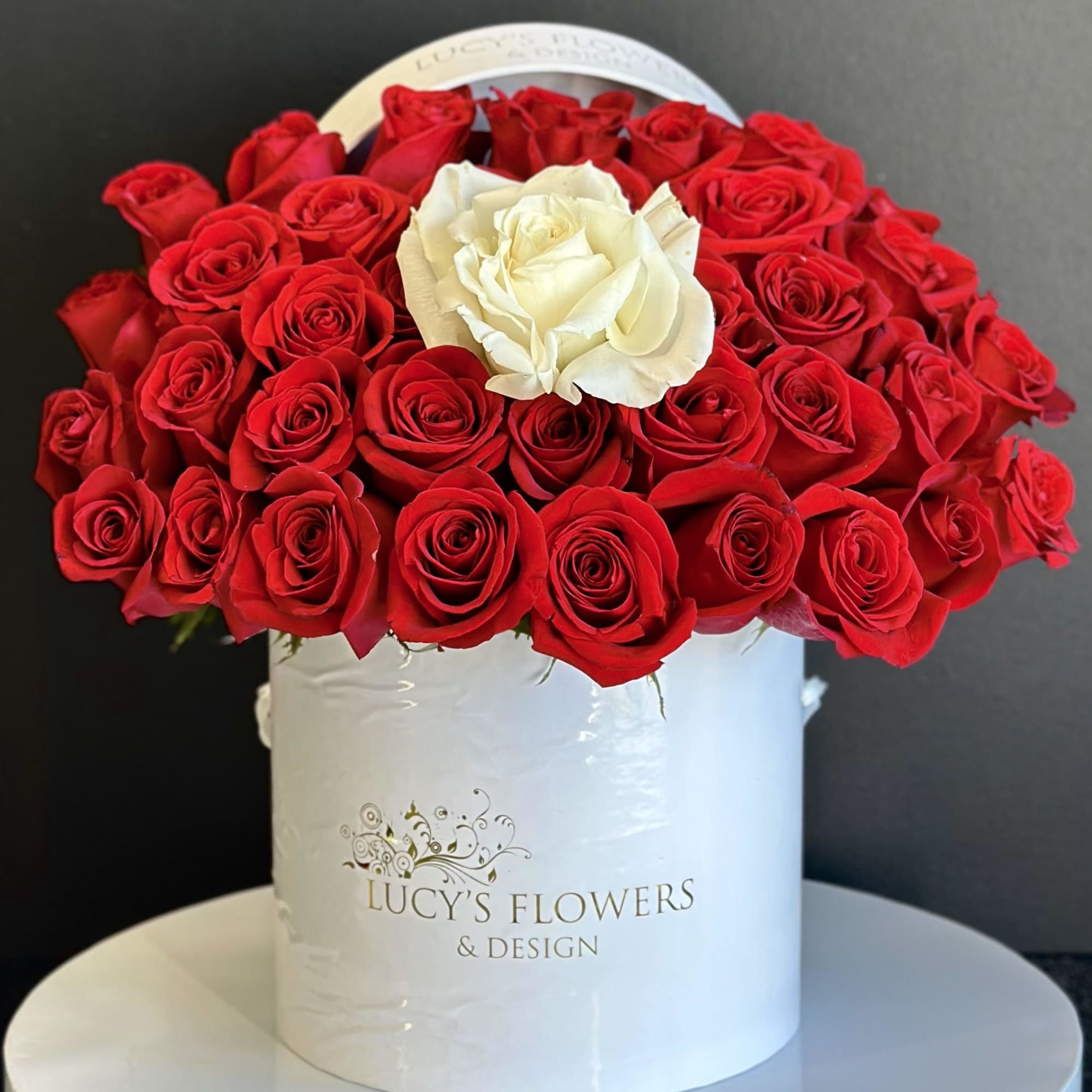 Red roses with one white rose in a white hatbox