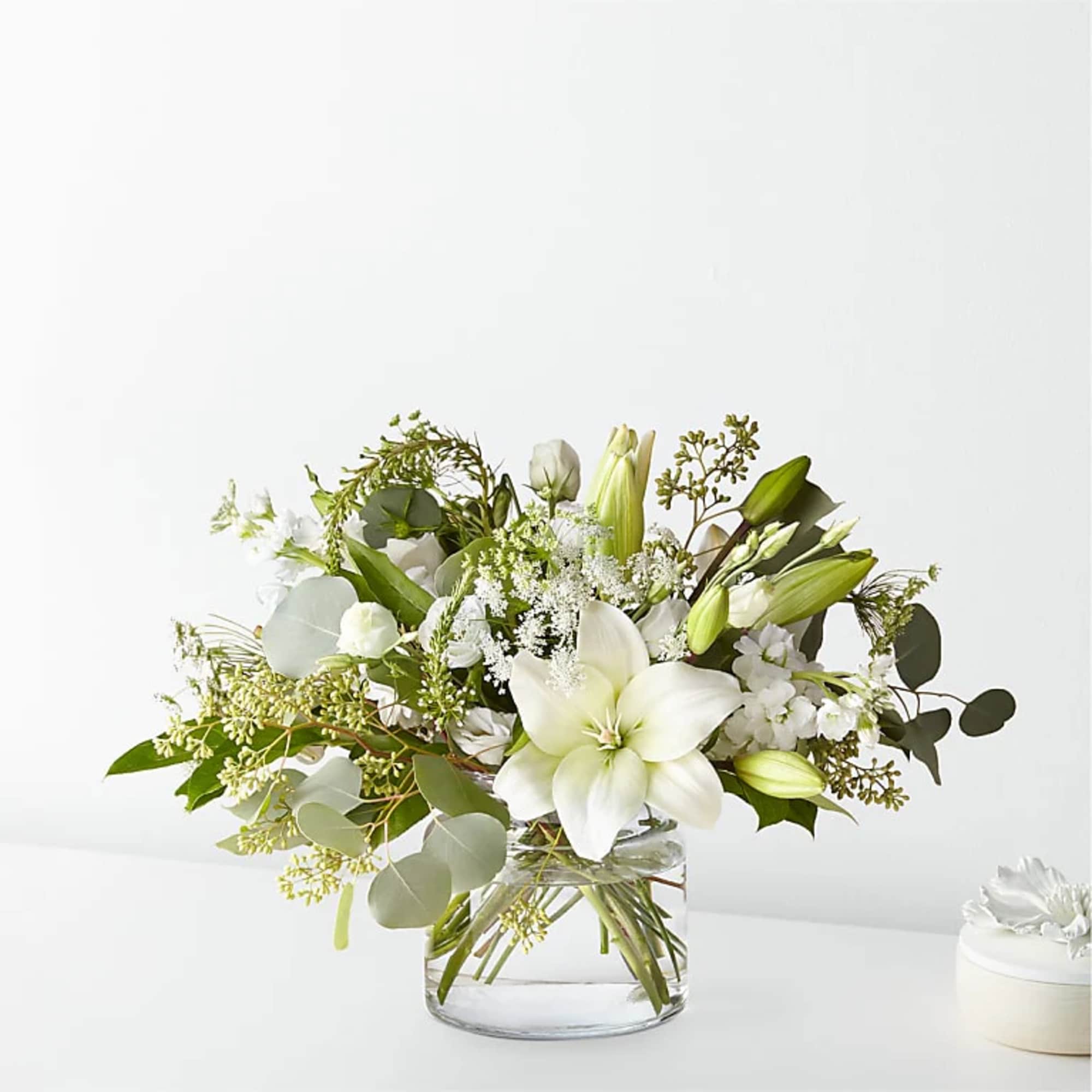 White lilies and small white flowers in a clear glass vase