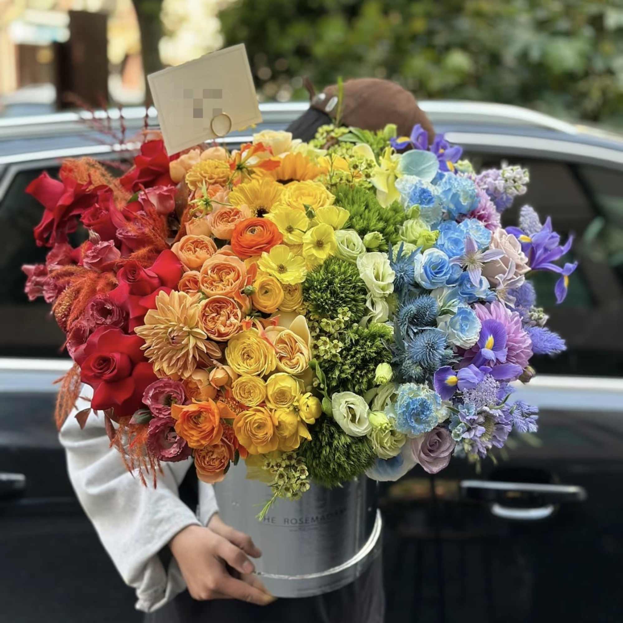 Large rainbow bouquet in a gray bucket with a card attached