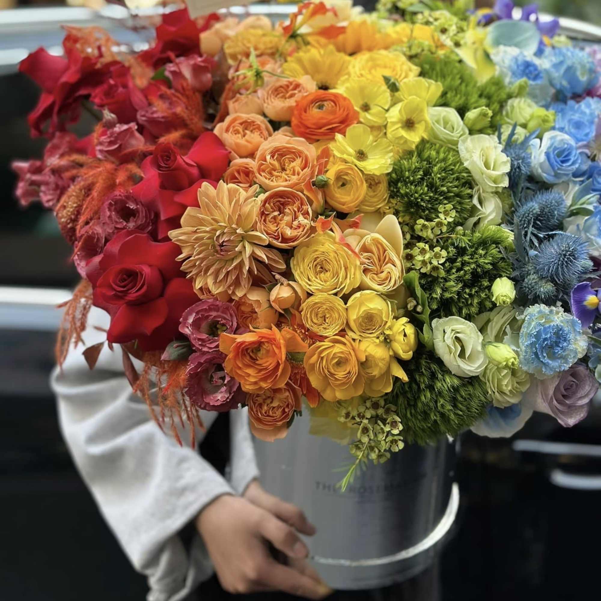 Rainbow bouquet of roses and mixed blooms in a gray bucket